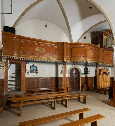 Zdjęcie nr 1: Chór muzyczny konstrukcji drewnianej, wsparty na dwóch ośmiobocznych kolumnach o trzonach dekorowanych płycinami wypełnionymi maswerkiem, ustawionych na wysokich cokołach. Parapet chóru muzycznego o linii wklęsło-wypukłej z wybrzuszoną częścią środkową. Balustrada pełna, dekorowana płycinami z umieszczonym w centrum złoconym geometrycznym ornamentem. W narożach płycin złocone rozetki. W dolnej części parapetu podwieszony złocony lambrekin, w górnej profilowany gzyms. Chór dostępny za pomocą drewnianych schodów w południowo-zachodnim narożniku nawy. Wejście ujęte parą lizen, w nadprożu ornament naśladujący podwieszoną kotarę. Struktura chóru malowana w odcieniach jasnego brązu z ciemnoczerwonymi elementami, ornamentyka złocona.