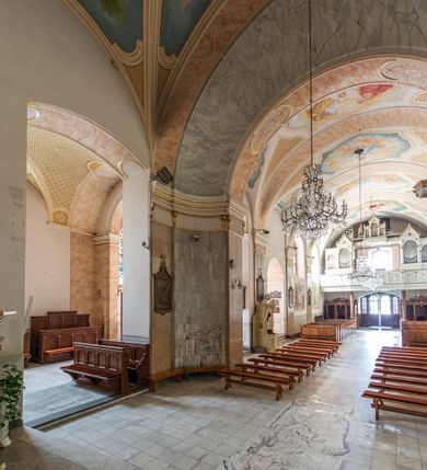 Zdjęcie nr 8: Po kilkukrotnych przekształceniach kościół składa się z prostokątnej, czteroprzęsłowej nawy głównej, dwóch, dwuprzęsłowych naw bocznych, przerobionych z dawnych kaplic i jednoprzęsłowego prezbiterium zamkniętego od wschodu apsydą. Na przedłużeniu apsydy otoczonej półkolistym aneksem wzniesiono czworoboczną, piętrową zakrystią. Od zachodu do nawy przylega wysunięta do przodu czworoboczna wieża o ściętych narożach z urządzoną w przyziemiu kruchtą. Wieża uzyskała trzy kondygnacje wyznaczone za pomocą profilowanych gzymsów. Środkowe piętro wieży połączono z bocznymi częściami fasady za pomocą wolut. Na dwóch pierwszych kondygnacjach ścięte naroża artykułowano za pomocą pilastrów o prostych głowicach. Pilastry drugiej kondygnacji ozdobiono krótkimi zwisami kampanul. Kondygnacja trzecia także została wzniesiona na rzucie czworoboku ale o wklęsłych narożach. Jej ściany flankują pary pilastrów o korynckich głowicach podtrzymujące imposty wspierające półkoliście wyłamane na osi belkowanie wspierające baniasty hełm z latarnią zwieńczony krzyżem z koroną. Pomiędzy impostami pod wyłamanym belkowaniem umieszczono tarcze zegarowe. Na trzeciej kondygnacji ponad belkowaniem od zachodu nadwieszono czworoboczny balkon z tralkową balustradą. Sześcioboczną sygnaturkę z latarnią zwieńczoną stożkowym hełmem z ustawioną na szczycie figurką Matki Boskiej Niepokalanie Poczętej zawieszono na siodłowym dachu kościoła w części wschodniej nawy głównej. Elewacje boczne kościoła rozczłonkowano za pomocą podziałów ramowych lub lizenowych. Wnętrze świątyni nakryto sklepieniem kolebkowym wspartym na gurtach, przechodzących na przyścienne pilastry podtrzymujące odcinki przerwanego belkowania. W ostanim zachodnim przęśle urządzono chór muzyczny wsparty na dwóch filarach z wypukłym na osi parapetem, artykułowanym za pomocą pilastrów i par arkadek. W prezbiterium ustawiono ołtarz główny oraz ambonę, a w nawach ołtarze boczne. 