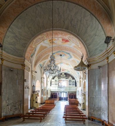 Zdjęcie nr 9: Po kilkukrotnych przekształceniach kościół składa się z prostokątnej, czteroprzęsłowej nawy głównej, dwóch, dwuprzęsłowych naw bocznych, przerobionych z dawnych kaplic i jednoprzęsłowego prezbiterium zamkniętego od wschodu apsydą. Na przedłużeniu apsydy otoczonej półkolistym aneksem wzniesiono czworoboczną, piętrową zakrystią. Od zachodu do nawy przylega wysunięta do przodu czworoboczna wieża o ściętych narożach z urządzoną w przyziemiu kruchtą. Wieża uzyskała trzy kondygnacje wyznaczone za pomocą profilowanych gzymsów. Środkowe piętro wieży połączono z bocznymi częściami fasady za pomocą wolut. Na dwóch pierwszych kondygnacjach ścięte naroża artykułowano za pomocą pilastrów o prostych głowicach. Pilastry drugiej kondygnacji ozdobiono krótkimi zwisami kampanul. Kondygnacja trzecia także została wzniesiona na rzucie czworoboku ale o wklęsłych narożach. Jej ściany flankują pary pilastrów o korynckich głowicach podtrzymujące imposty wspierające półkoliście wyłamane na osi belkowanie wspierające baniasty hełm z latarnią zwieńczony krzyżem z koroną. Pomiędzy impostami pod wyłamanym belkowaniem umieszczono tarcze zegarowe. Na trzeciej kondygnacji ponad belkowaniem od zachodu nadwieszono czworoboczny balkon z tralkową balustradą. Sześcioboczną sygnaturkę z latarnią zwieńczoną stożkowym hełmem z ustawioną na szczycie figurką Matki Boskiej Niepokalanie Poczętej zawieszono na siodłowym dachu kościoła w części wschodniej nawy głównej. Elewacje boczne kościoła rozczłonkowano za pomocą podziałów ramowych lub lizenowych. Wnętrze świątyni nakryto sklepieniem kolebkowym wspartym na gurtach, przechodzących na przyścienne pilastry podtrzymujące odcinki przerwanego belkowania. W ostanim zachodnim przęśle urządzono chór muzyczny wsparty na dwóch filarach z wypukłym na osi parapetem, artykułowanym za pomocą pilastrów i par arkadek. W prezbiterium ustawiono ołtarz główny oraz ambonę, a w nawach ołtarze boczne. 