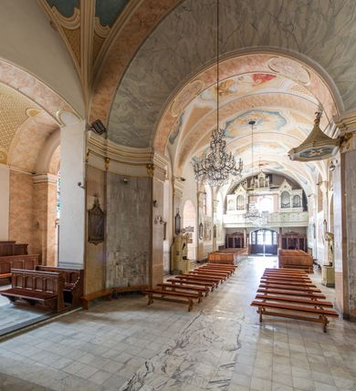 Zdjęcie nr 11: Po kilkukrotnych przekształceniach kościół składa się z prostokątnej, czteroprzęsłowej nawy głównej, dwóch, dwuprzęsłowych naw bocznych, przerobionych z dawnych kaplic i jednoprzęsłowego prezbiterium zamkniętego od wschodu apsydą. Na przedłużeniu apsydy otoczonej półkolistym aneksem wzniesiono czworoboczną, piętrową zakrystią. Od zachodu do nawy przylega wysunięta do przodu czworoboczna wieża o ściętych narożach z urządzoną w przyziemiu kruchtą. Wieża uzyskała trzy kondygnacje wyznaczone za pomocą profilowanych gzymsów. Środkowe piętro wieży połączono z bocznymi częściami fasady za pomocą wolut. Na dwóch pierwszych kondygnacjach ścięte naroża artykułowano za pomocą pilastrów o prostych głowicach. Pilastry drugiej kondygnacji ozdobiono krótkimi zwisami kampanul. Kondygnacja trzecia także została wzniesiona na rzucie czworoboku ale o wklęsłych narożach. Jej ściany flankują pary pilastrów o korynckich głowicach podtrzymujące imposty wspierające półkoliście wyłamane na osi belkowanie wspierające baniasty hełm z latarnią zwieńczony krzyżem z koroną. Pomiędzy impostami pod wyłamanym belkowaniem umieszczono tarcze zegarowe. Na trzeciej kondygnacji ponad belkowaniem od zachodu nadwieszono czworoboczny balkon z tralkową balustradą. Sześcioboczną sygnaturkę z latarnią zwieńczoną stożkowym hełmem z ustawioną na szczycie figurką Matki Boskiej Niepokalanie Poczętej zawieszono na siodłowym dachu kościoła w części wschodniej nawy głównej. Elewacje boczne kościoła rozczłonkowano za pomocą podziałów ramowych lub lizenowych. Wnętrze świątyni nakryto sklepieniem kolebkowym wspartym na gurtach, przechodzących na przyścienne pilastry podtrzymujące odcinki przerwanego belkowania. W ostanim zachodnim przęśle urządzono chór muzyczny wsparty na dwóch filarach z wypukłym na osi parapetem, artykułowanym za pomocą pilastrów i par arkadek. W prezbiterium ustawiono ołtarz główny oraz ambonę, a w nawach ołtarze boczne. 