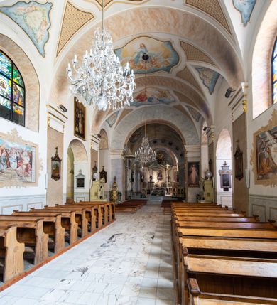 Zdjęcie nr 15: Po kilkukrotnych przekształceniach kościół składa się z prostokątnej, czteroprzęsłowej nawy głównej, dwóch, dwuprzęsłowych naw bocznych, przerobionych z dawnych kaplic i jednoprzęsłowego prezbiterium zamkniętego od wschodu apsydą. Na przedłużeniu apsydy otoczonej półkolistym aneksem wzniesiono czworoboczną, piętrową zakrystią. Od zachodu do nawy przylega wysunięta do przodu czworoboczna wieża o ściętych narożach z urządzoną w przyziemiu kruchtą. Wieża uzyskała trzy kondygnacje wyznaczone za pomocą profilowanych gzymsów. Środkowe piętro wieży połączono z bocznymi częściami fasady za pomocą wolut. Na dwóch pierwszych kondygnacjach ścięte naroża artykułowano za pomocą pilastrów o prostych głowicach. Pilastry drugiej kondygnacji ozdobiono krótkimi zwisami kampanul. Kondygnacja trzecia także została wzniesiona na rzucie czworoboku ale o wklęsłych narożach. Jej ściany flankują pary pilastrów o korynckich głowicach podtrzymujące imposty wspierające półkoliście wyłamane na osi belkowanie wspierające baniasty hełm z latarnią zwieńczony krzyżem z koroną. Pomiędzy impostami pod wyłamanym belkowaniem umieszczono tarcze zegarowe. Na trzeciej kondygnacji ponad belkowaniem od zachodu nadwieszono czworoboczny balkon z tralkową balustradą. Sześcioboczną sygnaturkę z latarnią zwieńczoną stożkowym hełmem z ustawioną na szczycie figurką Matki Boskiej Niepokalanie Poczętej zawieszono na siodłowym dachu kościoła w części wschodniej nawy głównej. Elewacje boczne kościoła rozczłonkowano za pomocą podziałów ramowych lub lizenowych. Wnętrze świątyni nakryto sklepieniem kolebkowym wspartym na gurtach, przechodzących na przyścienne pilastry podtrzymujące odcinki przerwanego belkowania. W ostanim zachodnim przęśle urządzono chór muzyczny wsparty na dwóch filarach z wypukłym na osi parapetem, artykułowanym za pomocą pilastrów i par arkadek. W prezbiterium ustawiono ołtarz główny oraz ambonę, a w nawach ołtarze boczne. 