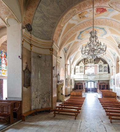 Zdjęcie nr 20: Po kilkukrotnych przekształceniach kościół składa się z prostokątnej, czteroprzęsłowej nawy głównej, dwóch, dwuprzęsłowych naw bocznych, przerobionych z dawnych kaplic i jednoprzęsłowego prezbiterium zamkniętego od wschodu apsydą. Na przedłużeniu apsydy otoczonej półkolistym aneksem wzniesiono czworoboczną, piętrową zakrystią. Od zachodu do nawy przylega wysunięta do przodu czworoboczna wieża o ściętych narożach z urządzoną w przyziemiu kruchtą. Wieża uzyskała trzy kondygnacje wyznaczone za pomocą profilowanych gzymsów. Środkowe piętro wieży połączono z bocznymi częściami fasady za pomocą wolut. Na dwóch pierwszych kondygnacjach ścięte naroża artykułowano za pomocą pilastrów o prostych głowicach. Pilastry drugiej kondygnacji ozdobiono krótkimi zwisami kampanul. Kondygnacja trzecia także została wzniesiona na rzucie czworoboku ale o wklęsłych narożach. Jej ściany flankują pary pilastrów o korynckich głowicach podtrzymujące imposty wspierające półkoliście wyłamane na osi belkowanie wspierające baniasty hełm z latarnią zwieńczony krzyżem z koroną. Pomiędzy impostami pod wyłamanym belkowaniem umieszczono tarcze zegarowe. Na trzeciej kondygnacji ponad belkowaniem od zachodu nadwieszono czworoboczny balkon z tralkową balustradą. Sześcioboczną sygnaturkę z latarnią zwieńczoną stożkowym hełmem z ustawioną na szczycie figurką Matki Boskiej Niepokalanie Poczętej zawieszono na siodłowym dachu kościoła w części wschodniej nawy głównej. Elewacje boczne kościoła rozczłonkowano za pomocą podziałów ramowych lub lizenowych. Wnętrze świątyni nakryto sklepieniem kolebkowym wspartym na gurtach, przechodzących na przyścienne pilastry podtrzymujące odcinki przerwanego belkowania. W ostanim zachodnim przęśle urządzono chór muzyczny wsparty na dwóch filarach z wypukłym na osi parapetem, artykułowanym za pomocą pilastrów i par arkadek. W prezbiterium ustawiono ołtarz główny oraz ambonę, a w nawach ołtarze boczne. 