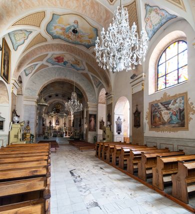 Zdjęcie nr 21: Po kilkukrotnych przekształceniach kościół składa się z prostokątnej, czteroprzęsłowej nawy głównej, dwóch, dwuprzęsłowych naw bocznych, przerobionych z dawnych kaplic i jednoprzęsłowego prezbiterium zamkniętego od wschodu apsydą. Na przedłużeniu apsydy otoczonej półkolistym aneksem wzniesiono czworoboczną, piętrową zakrystią. Od zachodu do nawy przylega wysunięta do przodu czworoboczna wieża o ściętych narożach z urządzoną w przyziemiu kruchtą. Wieża uzyskała trzy kondygnacje wyznaczone za pomocą profilowanych gzymsów. Środkowe piętro wieży połączono z bocznymi częściami fasady za pomocą wolut. Na dwóch pierwszych kondygnacjach ścięte naroża artykułowano za pomocą pilastrów o prostych głowicach. Pilastry drugiej kondygnacji ozdobiono krótkimi zwisami kampanul. Kondygnacja trzecia także została wzniesiona na rzucie czworoboku ale o wklęsłych narożach. Jej ściany flankują pary pilastrów o korynckich głowicach podtrzymujące imposty wspierające półkoliście wyłamane na osi belkowanie wspierające baniasty hełm z latarnią zwieńczony krzyżem z koroną. Pomiędzy impostami pod wyłamanym belkowaniem umieszczono tarcze zegarowe. Na trzeciej kondygnacji ponad belkowaniem od zachodu nadwieszono czworoboczny balkon z tralkową balustradą. Sześcioboczną sygnaturkę z latarnią zwieńczoną stożkowym hełmem z ustawioną na szczycie figurką Matki Boskiej Niepokalanie Poczętej zawieszono na siodłowym dachu kościoła w części wschodniej nawy głównej. Elewacje boczne kościoła rozczłonkowano za pomocą podziałów ramowych lub lizenowych. Wnętrze świątyni nakryto sklepieniem kolebkowym wspartym na gurtach, przechodzących na przyścienne pilastry podtrzymujące odcinki przerwanego belkowania. W ostanim zachodnim przęśle urządzono chór muzyczny wsparty na dwóch filarach z wypukłym na osi parapetem, artykułowanym za pomocą pilastrów i par arkadek. W prezbiterium ustawiono ołtarz główny oraz ambonę, a w nawach ołtarze boczne. 