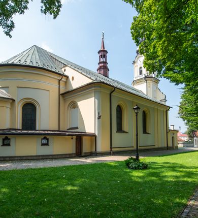 Zdjęcie nr 13: Po kilkukrotnych przekształceniach kościół składa się z prostokątnej, czteroprzęsłowej nawy głównej, dwóch, dwuprzęsłowych naw bocznych, przerobionych z dawnych kaplic i jednoprzęsłowego prezbiterium zamkniętego od wschodu apsydą. Na przedłużeniu apsydy otoczonej półkolistym aneksem wzniesiono czworoboczną, piętrową zakrystią. Od zachodu do nawy przylega wysunięta do przodu czworoboczna wieża o ściętych narożach z urządzoną w przyziemiu kruchtą. Wieża uzyskała trzy kondygnacje wyznaczone za pomocą profilowanych gzymsów. Środkowe piętro wieży połączono z bocznymi częściami fasady za pomocą wolut. Na dwóch pierwszych kondygnacjach ścięte naroża artykułowano za pomocą pilastrów o prostych głowicach. Pilastry drugiej kondygnacji ozdobiono krótkimi zwisami kampanul. Kondygnacja trzecia także została wzniesiona na rzucie czworoboku ale o wklęsłych narożach. Jej ściany flankują pary pilastrów o korynckich głowicach podtrzymujące imposty wspierające półkoliście wyłamane na osi belkowanie wspierające baniasty hełm z latarnią zwieńczony krzyżem z koroną. Pomiędzy impostami pod wyłamanym belkowaniem umieszczono tarcze zegarowe. Na trzeciej kondygnacji ponad belkowaniem od zachodu nadwieszono czworoboczny balkon z tralkową balustradą. Sześcioboczną sygnaturkę z latarnią zwieńczoną stożkowym hełmem z ustawioną na szczycie figurką Matki Boskiej Niepokalanie Poczętej zawieszono na siodłowym dachu kościoła w części wschodniej nawy głównej. Elewacje boczne kościoła rozczłonkowano za pomocą podziałów ramowych lub lizenowych. Wnętrze świątyni nakryto sklepieniem kolebkowym wspartym na gurtach, przechodzących na przyścienne pilastry podtrzymujące odcinki przerwanego belkowania. W ostanim zachodnim przęśle urządzono chór muzyczny wsparty na dwóch filarach z wypukłym na osi parapetem, artykułowanym za pomocą pilastrów i par arkadek. W prezbiterium ustawiono ołtarz główny oraz ambonę, a w nawach ołtarze boczne. 