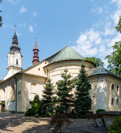 Zdjęcie nr 1: Po kilkukrotnych przekształceniach kościół składa się z prostokątnej, czteroprzęsłowej nawy głównej, dwóch, dwuprzęsłowych naw bocznych, przerobionych z dawnych kaplic i jednoprzęsłowego prezbiterium zamkniętego od wschodu apsydą. Na przedłużeniu apsydy otoczonej półkolistym aneksem wzniesiono czworoboczną, piętrową zakrystią. Od zachodu do nawy przylega wysunięta do przodu czworoboczna wieża o ściętych narożach z urządzoną w przyziemiu kruchtą. Wieża uzyskała trzy kondygnacje wyznaczone za pomocą profilowanych gzymsów. Środkowe piętro wieży połączono z bocznymi częściami fasady za pomocą wolut. Na dwóch pierwszych kondygnacjach ścięte naroża artykułowano za pomocą pilastrów o prostych głowicach. Pilastry drugiej kondygnacji ozdobiono krótkimi zwisami kampanul. Kondygnacja trzecia także została wzniesiona na rzucie czworoboku ale o wklęsłych narożach. Jej ściany flankują pary pilastrów o korynckich głowicach podtrzymujące imposty wspierające półkoliście wyłamane na osi belkowanie wspierające baniasty hełm z latarnią zwieńczony krzyżem z koroną. Pomiędzy impostami pod wyłamanym belkowaniem umieszczono tarcze zegarowe. Na trzeciej kondygnacji ponad belkowaniem od zachodu nadwieszono czworoboczny balkon z tralkową balustradą. Sześcioboczną sygnaturkę z latarnią zwieńczoną stożkowym hełmem z ustawioną na szczycie figurką Matki Boskiej Niepokalanie Poczętej zawieszono na siodłowym dachu kościoła w części wschodniej nawy głównej. Elewacje boczne kościoła rozczłonkowano za pomocą podziałów ramowych lub lizenowych. Wnętrze świątyni nakryto sklepieniem kolebkowym wspartym na gurtach, przechodzących na przyścienne pilastry podtrzymujące odcinki przerwanego belkowania. W ostanim zachodnim przęśle urządzono chór muzyczny wsparty na dwóch filarach z wypukłym na osi parapetem, artykułowanym za pomocą pilastrów i par arkadek. W prezbiterium ustawiono ołtarz główny oraz ambonę, a w nawach ołtarze boczne. 