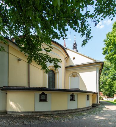 Zdjęcie nr 25: Po kilkukrotnych przekształceniach kościół składa się z prostokątnej, czteroprzęsłowej nawy głównej, dwóch, dwuprzęsłowych naw bocznych, przerobionych z dawnych kaplic i jednoprzęsłowego prezbiterium zamkniętego od wschodu apsydą. Na przedłużeniu apsydy otoczonej półkolistym aneksem wzniesiono czworoboczną, piętrową zakrystią. Od zachodu do nawy przylega wysunięta do przodu czworoboczna wieża o ściętych narożach z urządzoną w przyziemiu kruchtą. Wieża uzyskała trzy kondygnacje wyznaczone za pomocą profilowanych gzymsów. Środkowe piętro wieży połączono z bocznymi częściami fasady za pomocą wolut. Na dwóch pierwszych kondygnacjach ścięte naroża artykułowano za pomocą pilastrów o prostych głowicach. Pilastry drugiej kondygnacji ozdobiono krótkimi zwisami kampanul. Kondygnacja trzecia także została wzniesiona na rzucie czworoboku ale o wklęsłych narożach. Jej ściany flankują pary pilastrów o korynckich głowicach podtrzymujące imposty wspierające półkoliście wyłamane na osi belkowanie wspierające baniasty hełm z latarnią zwieńczony krzyżem z koroną. Pomiędzy impostami pod wyłamanym belkowaniem umieszczono tarcze zegarowe. Na trzeciej kondygnacji ponad belkowaniem od zachodu nadwieszono czworoboczny balkon z tralkową balustradą. Sześcioboczną sygnaturkę z latarnią zwieńczoną stożkowym hełmem z ustawioną na szczycie figurką Matki Boskiej Niepokalanie Poczętej zawieszono na siodłowym dachu kościoła w części wschodniej nawy głównej. Elewacje boczne kościoła rozczłonkowano za pomocą podziałów ramowych lub lizenowych. Wnętrze świątyni nakryto sklepieniem kolebkowym wspartym na gurtach, przechodzących na przyścienne pilastry podtrzymujące odcinki przerwanego belkowania. W ostanim zachodnim przęśle urządzono chór muzyczny wsparty na dwóch filarach z wypukłym na osi parapetem, artykułowanym za pomocą pilastrów i par arkadek. W prezbiterium ustawiono ołtarz główny oraz ambonę, a w nawach ołtarze boczne. 