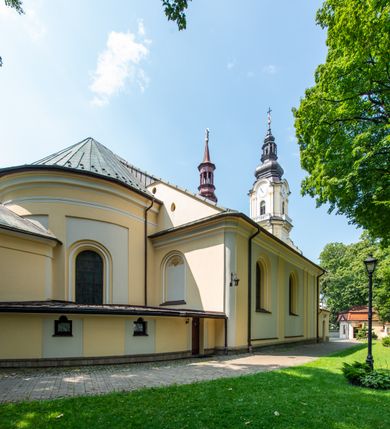 Zdjęcie nr 24: Po kilkukrotnych przekształceniach kościół składa się z prostokątnej, czteroprzęsłowej nawy głównej, dwóch, dwuprzęsłowych naw bocznych, przerobionych z dawnych kaplic i jednoprzęsłowego prezbiterium zamkniętego od wschodu apsydą. Na przedłużeniu apsydy otoczonej półkolistym aneksem wzniesiono czworoboczną, piętrową zakrystią. Od zachodu do nawy przylega wysunięta do przodu czworoboczna wieża o ściętych narożach z urządzoną w przyziemiu kruchtą. Wieża uzyskała trzy kondygnacje wyznaczone za pomocą profilowanych gzymsów. Środkowe piętro wieży połączono z bocznymi częściami fasady za pomocą wolut. Na dwóch pierwszych kondygnacjach ścięte naroża artykułowano za pomocą pilastrów o prostych głowicach. Pilastry drugiej kondygnacji ozdobiono krótkimi zwisami kampanul. Kondygnacja trzecia także została wzniesiona na rzucie czworoboku ale o wklęsłych narożach. Jej ściany flankują pary pilastrów o korynckich głowicach podtrzymujące imposty wspierające półkoliście wyłamane na osi belkowanie wspierające baniasty hełm z latarnią zwieńczony krzyżem z koroną. Pomiędzy impostami pod wyłamanym belkowaniem umieszczono tarcze zegarowe. Na trzeciej kondygnacji ponad belkowaniem od zachodu nadwieszono czworoboczny balkon z tralkową balustradą. Sześcioboczną sygnaturkę z latarnią zwieńczoną stożkowym hełmem z ustawioną na szczycie figurką Matki Boskiej Niepokalanie Poczętej zawieszono na siodłowym dachu kościoła w części wschodniej nawy głównej. Elewacje boczne kościoła rozczłonkowano za pomocą podziałów ramowych lub lizenowych. Wnętrze świątyni nakryto sklepieniem kolebkowym wspartym na gurtach, przechodzących na przyścienne pilastry podtrzymujące odcinki przerwanego belkowania. W ostanim zachodnim przęśle urządzono chór muzyczny wsparty na dwóch filarach z wypukłym na osi parapetem, artykułowanym za pomocą pilastrów i par arkadek. W prezbiterium ustawiono ołtarz główny oraz ambonę, a w nawach ołtarze boczne. 