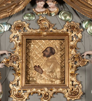 Zdjęcie nr 46: Nastawa niearchitektoniczna w formie paludamentu. Mensa kamienna, oparta na dwóch kamiennych pilastrach o kanelowanych trzonach, ustawionych na cokolikach. Na mensie  tabernakulum w formie drewnianej skrzynki na czterech nóżkach, zakończone gzymsem, o drzwiczkach w kształcie stojącego prostokąta o ściętych górnych narożach, ujęte profilowaną ramą z przedstawieniem kielicha z hostią w glorii. Na nim tron wystawienia na relikwiarz. Tabernakulum flankują dwie figury aniołów ustawione na cokołach. 
Paludament podwiązany po bokach sznurem z chwostami, podtrzymywany przez putta, lamowany frędzlą, zwieńczony baldachimem utworzonym z fragmentu wklęsło-wypukłego gzymsu z lambrekinem. W polu wnęka w kształcie stojącego prostokąta ujęta profilowaną ramą i rocaille'm, z obrazem św. Karola Boromeusza. Nad obrazem rzeźbione obłoki i dwie uskrzydlone główki anielskie, po bokach nadlatujące dwa putta. Paludament polichromowany wewnątrz w kolorze szaro-brązowym, zewnątrz złocony.