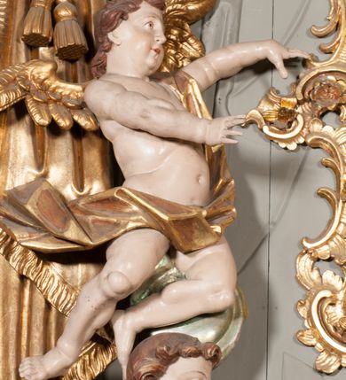 Zdjęcie nr 25: Nastawa niearchitektoniczna w formie paludamentu. Mensa kamienna, oparta na dwóch kamiennych pilastrach o kanelowanych trzonach, ustawionych na cokolikach. Na mensie  tabernakulum w formie drewnianej skrzynki na czterech nóżkach, zakończone gzymsem, o drzwiczkach w kształcie stojącego prostokąta o ściętych górnych narożach, ujęte profilowaną ramą z przedstawieniem kielicha z hostią w glorii. Na nim tron wystawienia na relikwiarz. Tabernakulum flankują dwie figury aniołów ustawione na cokołach. 
Paludament podwiązany po bokach sznurem z chwostami, podtrzymywany przez putta, lamowany frędzlą, zwieńczony baldachimem utworzonym z fragmentu wklęsło-wypukłego gzymsu z lambrekinem. W polu wnęka w kształcie stojącego prostokąta ujęta profilowaną ramą i rocaille'm, z obrazem św. Karola Boromeusza. Nad obrazem rzeźbione obłoki i dwie uskrzydlone główki anielskie, po bokach nadlatujące dwa putta. Paludament polichromowany wewnątrz w kolorze szaro-brązowym, zewnątrz złocony.