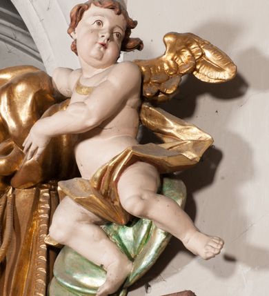 Zdjęcie nr 30: Nastawa niearchitektoniczna w formie paludamentu. Mensa kamienna, oparta na dwóch kamiennych pilastrach o kanelowanych trzonach, ustawionych na cokolikach. Na mensie  tabernakulum w formie drewnianej skrzynki na czterech nóżkach, zakończone gzymsem, o drzwiczkach w kształcie stojącego prostokąta o ściętych górnych narożach, ujęte profilowaną ramą z przedstawieniem kielicha z hostią w glorii. Na nim tron wystawienia na relikwiarz. Tabernakulum flankują dwie figury aniołów ustawione na cokołach. 
Paludament podwiązany po bokach sznurem z chwostami, podtrzymywany przez putta, lamowany frędzlą, zwieńczony baldachimem utworzonym z fragmentu wklęsło-wypukłego gzymsu z lambrekinem. W polu wnęka w kształcie stojącego prostokąta ujęta profilowaną ramą i rocaille'm, z obrazem św. Karola Boromeusza. Nad obrazem rzeźbione obłoki i dwie uskrzydlone główki anielskie, po bokach nadlatujące dwa putta. Paludament polichromowany wewnątrz w kolorze szaro-brązowym, zewnątrz złocony.