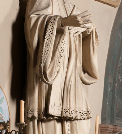 Zdjęcie nr 10: Pełnoplastyczna rzeźba ustawiona na czworobocznym, niskim postumencie wspartym na przyściennej, wolutowej konsoli przedstawia w całej postaci ujętego w nieznacznym kontrapoście księdza. Duchowny prawą rękę ma odsuniętą od siebie, lewą zaś przykłada do piersi. Jest to młody mężczyzna z uniesioną głową i spojrzeniem skierowanym w niebo. Ma owalną twarz z wydatnym nosem i ustami pozbawioną zarostu oraz krótkie włosy odsłaniające uszy. Duchowny ubrany jest w sutannę, z wysoką koloratką, komżę wiązaną pod szyją z szerokimi rękawami, obszytą koronką oraz nałożoną na ramionach stułę. Spod sutanny widać trzewiki. Rzeźba w całości polichromowana jest na biało. Na postumencie wyryta data 1797. 