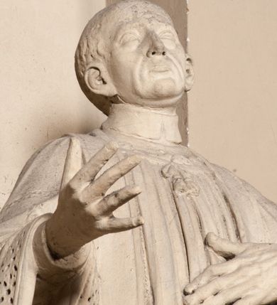 Zdjęcie nr 11: Pełnoplastyczna rzeźba ustawiona na czworobocznym, niskim postumencie wspartym na przyściennej, wolutowej konsoli przedstawia w całej postaci ujętego w nieznacznym kontrapoście księdza. Duchowny prawą rękę ma odsuniętą od siebie, lewą zaś przykłada do piersi. Jest to młody mężczyzna z uniesioną głową i spojrzeniem skierowanym w niebo. Ma owalną twarz z wydatnym nosem i ustami pozbawioną zarostu oraz krótkie włosy odsłaniające uszy. Duchowny ubrany jest w sutannę, z wysoką koloratką, komżę wiązaną pod szyją z szerokimi rękawami, obszytą koronką oraz nałożoną na ramionach stułę. Spod sutanny widać trzewiki. Rzeźba w całości polichromowana jest na biało. Na postumencie wyryta data 1797. 