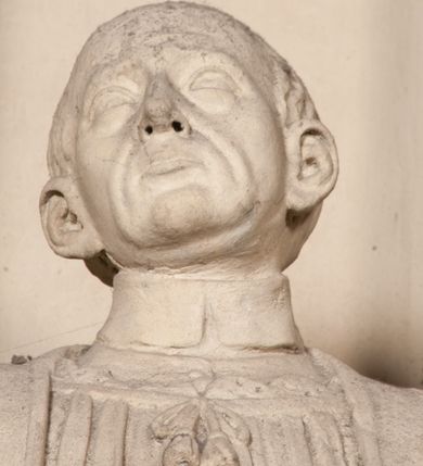 Zdjęcie nr 12: Pełnoplastyczna rzeźba ustawiona na czworobocznym, niskim postumencie wspartym na przyściennej, wolutowej konsoli przedstawia w całej postaci ujętego w nieznacznym kontrapoście księdza. Duchowny prawą rękę ma odsuniętą od siebie, lewą zaś przykłada do piersi. Jest to młody mężczyzna z uniesioną głową i spojrzeniem skierowanym w niebo. Ma owalną twarz z wydatnym nosem i ustami pozbawioną zarostu oraz krótkie włosy odsłaniające uszy. Duchowny ubrany jest w sutannę, z wysoką koloratką, komżę wiązaną pod szyją z szerokimi rękawami, obszytą koronką oraz nałożoną na ramionach stułę. Spod sutanny widać trzewiki. Rzeźba w całości polichromowana jest na biało. Na postumencie wyryta data 1797. 