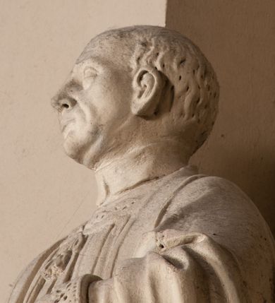 Zdjęcie nr 13: Pełnoplastyczna rzeźba ustawiona na czworobocznym, niskim postumencie wspartym na przyściennej, wolutowej konsoli przedstawia w całej postaci ujętego w nieznacznym kontrapoście księdza. Duchowny prawą rękę ma odsuniętą od siebie, lewą zaś przykłada do piersi. Jest to młody mężczyzna z uniesioną głową i spojrzeniem skierowanym w niebo. Ma owalną twarz z wydatnym nosem i ustami pozbawioną zarostu oraz krótkie włosy odsłaniające uszy. Duchowny ubrany jest w sutannę, z wysoką koloratką, komżę wiązaną pod szyją z szerokimi rękawami, obszytą koronką oraz nałożoną na ramionach stułę. Spod sutanny widać trzewiki. Rzeźba w całości polichromowana jest na biało. Na postumencie wyryta data 1797. 