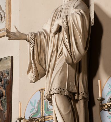 Zdjęcie nr 5: Pełnoplastyczna rzeźba ustawiona na czworobocznym, niskim postumencie wspartym na przyściennej, wolutowej konsoli przedstawia w całej postaci ujętego w nieznacznym kontrapoście księdza. Duchowny prawą rękę ma odsuniętą od siebie, lewą zaś przykłada do piersi. Jest to młody mężczyzna z uniesioną głową i spojrzeniem skierowanym w niebo. Ma owalną twarz z wydatnym nosem i ustami pozbawioną zarostu oraz krótkie włosy odsłaniające uszy. Duchowny ubrany jest w sutannę, z wysoką koloratką, komżę wiązaną pod szyją z szerokimi rękawami, obszytą koronką oraz nałożoną na ramionach stułę. Spod sutanny widać trzewiki. Rzeźba w całości polichromowana jest na biało. Na postumencie wyryta data 1797. 