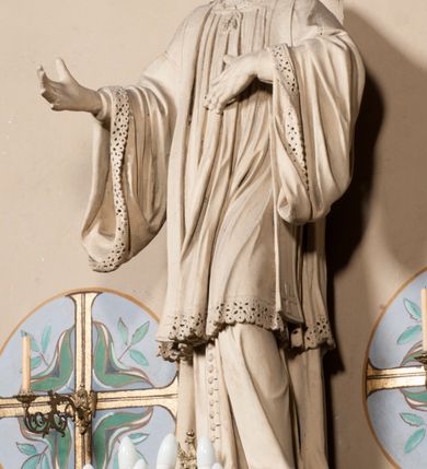 Zdjęcie nr 4: Pełnoplastyczna rzeźba ustawiona na czworobocznym, niskim postumencie wspartym na przyściennej, wolutowej konsoli przedstawia w całej postaci ujętego w nieznacznym kontrapoście księdza. Duchowny prawą rękę ma odsuniętą od siebie, lewą zaś przykłada do piersi. Jest to młody mężczyzna z uniesioną głową i spojrzeniem skierowanym w niebo. Ma owalną twarz z wydatnym nosem i ustami pozbawioną zarostu oraz krótkie włosy odsłaniające uszy. Duchowny ubrany jest w sutannę, z wysoką koloratką, komżę wiązaną pod szyją z szerokimi rękawami, obszytą koronką oraz nałożoną na ramionach stułę. Spod sutanny widać trzewiki. Rzeźba w całości polichromowana jest na biało. Na postumencie wyryta data 1797. 