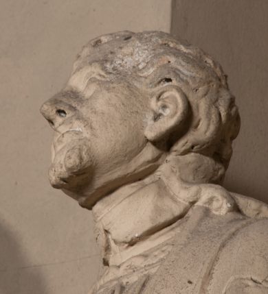 Zdjęcie nr 8: Pełnoplastyczna rzeźba ustawiona na czworobocznym, niskim postumencie wspartym na przyściennej, wolutowej konsoli przedstawia w całej postaci ujętego w nieznacznym kontrapoście księdza. Duchowny prawą rękę wznosi ku górze, lewą zaś odsuwa od siebie. Jest to młody mężczyzna z uniesioną głową i spojrzeniem skierowanym w niebo. Ma owalną twarz z wydatnym nosem i ustami okoloną krótkim zarostem i zmierzwionymi włosami odsłaniającymi uszy oraz spływającymi na ramiona. Duchowny ubrany jest w sutannę, z wysoką koloratką, komżę wiązaną pod szyją z szerokimi rękawami obszytą koronką oraz nałożoną na ramionach stułę. Spod sutanny widać trzewiki. Rzeźba w całości polichromowana jest na biało.