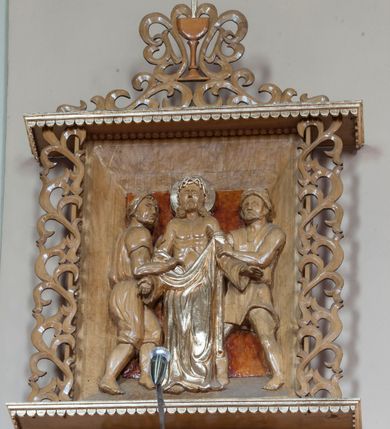 Zdjęcie nr 4: Stacje drogi krzyżowej w formie płaskorzeźbionych scen ujętych rozbudowanym obramieniem. Przedstawienia ograniczają się do najważniejszych osób, ukazanych w całej postaci i bliskim planie, na jednolitym, nieco ciemniejszym od reszty tle. Sposób ukazania postaci nosi cechy sztuki ludowej, ich pozy są sztywne, twarze zwrócone do widza, szaty marszczą się drobnymi fałdami. Postacie, ich ubrania oraz elementy scen zachowują naturalny kolor drewna, jedynie ubrania i nimb Chrystusa podkreślono złoceniem. Sceny zakomponowano w obramienie przypominające kapliczkę – na podstawie i pod daszkiem dekorowanymi lambrekinem, ujęte po bokach ażurową wicią roślinną. Poniżej podstawy numer sceny, a powyżej kielich z zatkniętym krzyżem łacińskim otacza i łączy w całość podobna wić. Lambrekin, krzyż oraz cyfry rzymskie złocone, reszta w kolorze naturalnego drewna. 