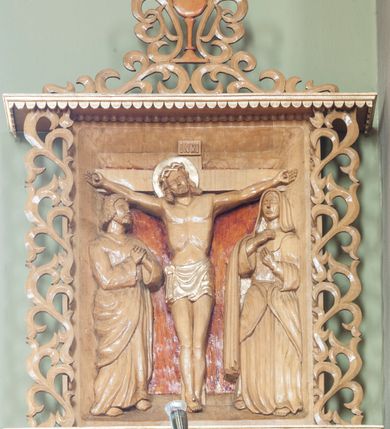 Zdjęcie nr 2: Stacje drogi krzyżowej w formie płaskorzeźbionych scen ujętych rozbudowanym obramieniem. Przedstawienia ograniczają się do najważniejszych osób, ukazanych w całej postaci i bliskim planie, na jednolitym, nieco ciemniejszym od reszty tle. Sposób ukazania postaci nosi cechy sztuki ludowej, ich pozy są sztywne, twarze zwrócone do widza, szaty marszczą się drobnymi fałdami. Postacie, ich ubrania oraz elementy scen zachowują naturalny kolor drewna, jedynie ubrania i nimb Chrystusa podkreślono złoceniem. Sceny zakomponowano w obramienie przypominające kapliczkę – na podstawie i pod daszkiem dekorowanymi lambrekinem, ujęte po bokach ażurową wicią roślinną. Poniżej podstawy numer sceny, a powyżej kielich z zatkniętym krzyżem łacińskim otacza i łączy w całość podobna wić. Lambrekin, krzyż oraz cyfry rzymskie złocone, reszta w kolorze naturalnego drewna. 