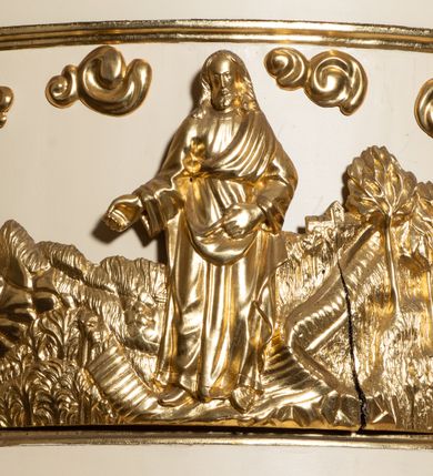 Zdjęcie nr 2: Przyścienna, wisząca z dostępem w formie jednobiegowych schodów od strony prezbiterium, ambona składa się z kosza, zaplecka i baldachimu. Kosz został wykonany na planie półkola ustawionego na niskim cokole z podwieszeniem w formie zbliżonej do stożka, ujętego wolutami i zakończonego wałkiem z szyszką. Jego boki podzielono pilastrami na nierówne pola, w których znajdują się płyciny z rozetami w zewnętrznych polach oraz w środkowym płaskorzeźbione przedstawienie Chrystusa siewcy na tle krajobrazu siewcy. Kosz zwieńczony został parapetem w formie gzymsu. Zaplecek ambony uzyskał formę stojącego prostokąta, ujętego lizenami ozdobionymi dekoracją geometryczną i roślinną. W polu umieszczono płaskorzeźbioną gołębicę Ducha Świętego w glorii promienistej. Baldachim wykonano na planie półkola w formie belkowania z podwieszonym lambrekinem i fryzem dekorowanym diagonalną kratownicą. Górę baldachimu opięto belkowaniem wyłamanym na dwóch osiach skrajnych. Baldachim wieńczy postument z leżącą na nim zamkniętą księgą z barankiem apokaliptycznym, stojącymi za nim dwiema tablicami Dekalogu oraz widniejącym nad nimi krzyżem w promienistej glorii. Architektura ambony została polichromowana na biało ze złoconymi profilami i ornamentyką oraz srebrzonymi detalami.