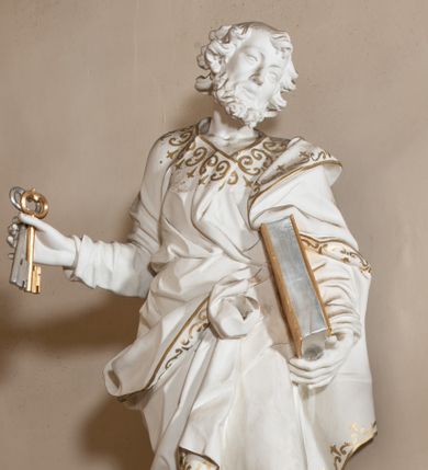 Zdjęcie nr 1: Rzeźba drążona z tyłu, stoi na prostokątnej podstawie ustawionej na wolutowej konsoli przyściennej. Postać apostoła jest ujęta frontalnie w kontrapoście z głową skierowaną i pochyloną w lewo. W prawej ręce odsuniętej od siebie apostoł trzyma klucze, a lewą podtrzymuje opartą o tors księgę. Piotr ma pociągłą, wychudzoną twarzą o migdałowatych oczach, małym nosie i pełnych ustach. Otacza ja krótka, kręcona broda i mocno kręcone włosy z łysiną na głowie. Postać ubrana jest w długą, przylegającą do ciała tunikę, przewiązaną w pasie oraz płaszcz zarzucony na lewe ramię, opadający na plecy, z fragmentem tkaniny przerzuconym przez prawe biodro, podwiązanym na wysokości pasa. Rzeźba została w całości polichromowana na biało ze złoconymi lamówkami szat i wzorem dekoracyjnym poprowadzonym wzdłuż krawędzi. Klucze i księga zostały wysrebrzone i wyzłocone.