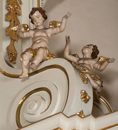 Zdjęcie nr 18: Dwukondygnacyjny, jednoosiowy ołtarz ze zwieńczeniem uzyskał strukturę architektoniczną. Stipes ołtarzowy wykonano w formie granitowego prostopadłościanu z mensą. Na mensie na osi ołtarza ustawiono tabernakulum z tronem wystawienia. Tabernakulum otrzymało kształt drewnianej skrzynki obitej blachą z drzwiczkami w formie stojącego prostokąta, z sześcioma kwaterami przedstawiającymi sceny z Pisma Świętego. Całość zamknięto silnie wysuniętym gzymsem wypukłym od frontu. Tron wystawienia utworzono w formie baldachimu ozdobionego lambrekinem z chwostami. Ujmują go spływy wolutowe z podwieszoną tkaniną, dekorowane liśćmi akantu. W przestrzeni zaplecka tronu umieszczono w promienistej glorii medalion z chrystogramem "IHS". Nastawa została ustawiona na wysokim cokole, zwieńczonym profilowanym gzymsem z wyodrębnionymi dwoma wspornikami skierowanymi do wewnątrz. Retabulum ujmuje  zwrócona na zewnątrz opilastrowana para filarów, przed którymi stoi para kolumn o kapitelach kompozytowych dźwigających pełne belkowanie wyłamane na ich osi. W polu centralnym znajduje się nisza w kształcie stojącego prostokąta zwieńczonego przerwanym prostokątnie łukiem półkolistym, nadwieszonym. Niszę obramienia profilowana rama. W jej wnętrzu znajduje się obraz Wniebowzięcia Najświętsze Marii Panny w drewnianych sukienkach wotywnych. Druga kondygnacja ujęta została dwiema parami zwróconych na zewnątrz pilastrów o trzonach przechodzących w spływy wolutowe. Pilastry dźwigają gzyms wyłamany na ich osi, który w części centralnej przyjmuje kształt spłaszczonego łuku. W polu umieszczono obraz z przedstawieniem Michała Archanioła w formie stojącego prostokąta o wklęsłych, dłuższych krawędziach oraz krótszych o kształcie łuku półkolistego nadwieszonego. Nastawa zakończona została okiem Opatrzności Bożej w glorii promienistej. Na cokole przed podporami ustawiono cztery figury adorujących aniołów. Ramę w polu środkowym udekorowano ornamentem roślinnym. W górnych przyłuczach umieszczono figury puttów na obłokach. Fryz został ozdobiony kwiatowymi girlandami. Centralnie na osi na gzymsie zawieszono kartusz z monogramem Marii w polu. Na zewnętrznych krawędziach belkowania pierwszej kondygnacji siedzą dwie figury aniołów, a na spływach wolutowych cztery putta. W trzonach pilastrów drugiej kondygnacji widoczne są zwisy z ornamentem kwiatowym podwieszonym na wstążce. W polu centralnym na dole umieszczono dwa wieńce, a u góry dwie uskrzydlone główki anielskie. Na belkowaniu znajdują się dwa putta na obłokach. Struktura nastawy została polichromowana w kolorze kości słoniowej, natomiast kolumny, pilastry, profile i ornamentyka zostały wyzłocone, a obłoki posrebrzone.