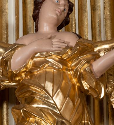 Zdjęcie nr 28: Dwukondygnacyjny, jednoosiowy ołtarz ze zwieńczeniem uzyskał strukturę architektoniczną. Stipes ołtarzowy wykonano w formie granitowego prostopadłościanu z mensą. Na mensie na osi ołtarza ustawiono tabernakulum z tronem wystawienia. Tabernakulum otrzymało kształt drewnianej skrzynki obitej blachą z drzwiczkami w formie stojącego prostokąta, z sześcioma kwaterami przedstawiającymi sceny z Pisma Świętego. Całość zamknięto silnie wysuniętym gzymsem wypukłym od frontu. Tron wystawienia utworzono w formie baldachimu ozdobionego lambrekinem z chwostami. Ujmują go spływy wolutowe z podwieszoną tkaniną, dekorowane liśćmi akantu. W przestrzeni zaplecka tronu umieszczono w promienistej glorii medalion z chrystogramem &quot;IHS&quot;. Nastawa została ustawiona na wysokim cokole, zwieńczonym profilowanym gzymsem z wyodrębnionymi dwoma wspornikami skierowanymi do wewnątrz. Retabulum ujmuje  zwrócona na zewnątrz opilastrowana para filarów, przed którymi stoi para kolumn o kapitelach kompozytowych dźwigających pełne belkowanie wyłamane na ich osi. W polu centralnym znajduje się nisza w kształcie stojącego prostokąta zwieńczonego przerwanym prostokątnie łukiem półkolistym, nadwieszonym. Niszę obramienia profilowana rama. W jej wnętrzu znajduje się obraz Wniebowzięcia Najświętsze Marii Panny w drewnianych sukienkach wotywnych. Druga kondygnacja ujęta została dwiema parami zwróconych na zewnątrz pilastrów o trzonach przechodzących w spływy wolutowe. Pilastry dźwigają gzyms wyłamany na ich osi, który w części centralnej przyjmuje kształt spłaszczonego łuku. W polu umieszczono obraz z przedstawieniem Michała Archanioła w formie stojącego prostokąta o wklęsłych, dłuższych krawędziach oraz krótszych o kształcie łuku półkolistego nadwieszonego. Nastawa zakończona została okiem Opatrzności Bożej w glorii promienistej. Na cokole przed podporami ustawiono cztery figury adorujących aniołów. Ramę w polu środkowym udekorowano ornamentem roślinnym. W górnych przyłuczach umieszczono figury puttów na obłokach. Fryz został ozdobiony kwiatowymi girlandami. Centralnie na osi na gzymsie zawieszono kartusz z monogramem Marii w polu. Na zewnętrznych krawędziach belkowania pierwszej kondygnacji siedzą dwie figury aniołów, a na spływach wolutowych cztery putta. W trzonach pilastrów drugiej kondygnacji widoczne są zwisy z ornamentem kwiatowym podwieszonym na wstążce. W polu centralnym na dole umieszczono dwa wieńce, a u góry dwie uskrzydlone główki anielskie. Na belkowaniu znajdują się dwa putta na obłokach. Struktura nastawy została polichromowana w kolorze kości słoniowej, natomiast kolumny, pilastry, profile i ornamentyka zostały wyzłocone, a obłoki posrebrzone.