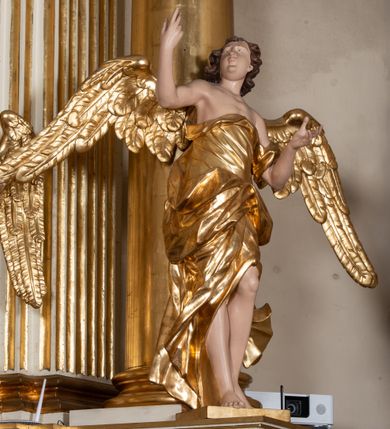 Zdjęcie nr 37: Dwukondygnacyjny, jednoosiowy ołtarz ze zwieńczeniem uzyskał strukturę architektoniczną. Stipes ołtarzowy wykonano w formie granitowego prostopadłościanu z mensą. Na mensie na osi ołtarza ustawiono tabernakulum z tronem wystawienia. Tabernakulum otrzymało kształt drewnianej skrzynki obitej blachą z drzwiczkami w formie stojącego prostokąta, z sześcioma kwaterami przedstawiającymi sceny z Pisma Świętego. Całość zamknięto silnie wysuniętym gzymsem wypukłym od frontu. Tron wystawienia utworzono w formie baldachimu ozdobionego lambrekinem z chwostami. Ujmują go spływy wolutowe z podwieszoną tkaniną, dekorowane liśćmi akantu. W przestrzeni zaplecka tronu umieszczono w promienistej glorii medalion z chrystogramem "IHS". Nastawa została ustawiona na wysokim cokole, zwieńczonym profilowanym gzymsem z wyodrębnionymi dwoma wspornikami skierowanymi do wewnątrz. Retabulum ujmuje  zwrócona na zewnątrz opilastrowana para filarów, przed którymi stoi para kolumn o kapitelach kompozytowych dźwigających pełne belkowanie wyłamane na ich osi. W polu centralnym znajduje się nisza w kształcie stojącego prostokąta zwieńczonego przerwanym prostokątnie łukiem półkolistym, nadwieszonym. Niszę obramienia profilowana rama. W jej wnętrzu znajduje się obraz Wniebowzięcia Najświętsze Marii Panny w drewnianych sukienkach wotywnych. Druga kondygnacja ujęta została dwiema parami zwróconych na zewnątrz pilastrów o trzonach przechodzących w spływy wolutowe. Pilastry dźwigają gzyms wyłamany na ich osi, który w części centralnej przyjmuje kształt spłaszczonego łuku. W polu umieszczono obraz z przedstawieniem Michała Archanioła w formie stojącego prostokąta o wklęsłych, dłuższych krawędziach oraz krótszych o kształcie łuku półkolistego nadwieszonego. Nastawa zakończona została okiem Opatrzności Bożej w glorii promienistej. Na cokole przed podporami ustawiono cztery figury adorujących aniołów. Ramę w polu środkowym udekorowano ornamentem roślinnym. W górnych przyłuczach umieszczono figury puttów na obłokach. Fryz został ozdobiony kwiatowymi girlandami. Centralnie na osi na gzymsie zawieszono kartusz z monogramem Marii w polu. Na zewnętrznych krawędziach belkowania pierwszej kondygnacji siedzą dwie figury aniołów, a na spływach wolutowych cztery putta. W trzonach pilastrów drugiej kondygnacji widoczne są zwisy z ornamentem kwiatowym podwieszonym na wstążce. W polu centralnym na dole umieszczono dwa wieńce, a u góry dwie uskrzydlone główki anielskie. Na belkowaniu znajdują się dwa putta na obłokach. Struktura nastawy została polichromowana w kolorze kości słoniowej, natomiast kolumny, pilastry, profile i ornamentyka zostały wyzłocone, a obłoki posrebrzone.