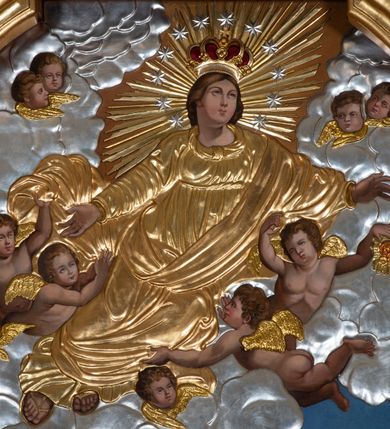 Zdjęcie nr 5: Dwukondygnacyjny, jednoosiowy ołtarz ze zwieńczeniem uzyskał strukturę architektoniczną. Stipes ołtarzowy wykonano w formie granitowego prostopadłościanu z mensą. Na mensie na osi ołtarza ustawiono tabernakulum z tronem wystawienia. Tabernakulum otrzymało kształt drewnianej skrzynki obitej blachą z drzwiczkami w formie stojącego prostokąta, z sześcioma kwaterami przedstawiającymi sceny z Pisma Świętego. Całość zamknięto silnie wysuniętym gzymsem wypukłym od frontu. Tron wystawienia utworzono w formie baldachimu ozdobionego lambrekinem z chwostami. Ujmują go spływy wolutowe z podwieszoną tkaniną, dekorowane liśćmi akantu. W przestrzeni zaplecka tronu umieszczono w promienistej glorii medalion z chrystogramem &quot;IHS&quot;. Nastawa została ustawiona na wysokim cokole, zwieńczonym profilowanym gzymsem z wyodrębnionymi dwoma wspornikami skierowanymi do wewnątrz. Retabulum ujmuje  zwrócona na zewnątrz opilastrowana para filarów, przed którymi stoi para kolumn o kapitelach kompozytowych dźwigających pełne belkowanie wyłamane na ich osi. W polu centralnym znajduje się nisza w kształcie stojącego prostokąta zwieńczonego przerwanym prostokątnie łukiem półkolistym, nadwieszonym. Niszę obramienia profilowana rama. W jej wnętrzu znajduje się obraz Wniebowzięcia Najświętsze Marii Panny w drewnianych sukienkach wotywnych. Druga kondygnacja ujęta została dwiema parami zwróconych na zewnątrz pilastrów o trzonach przechodzących w spływy wolutowe. Pilastry dźwigają gzyms wyłamany na ich osi, który w części centralnej przyjmuje kształt spłaszczonego łuku. W polu umieszczono obraz z przedstawieniem Michała Archanioła w formie stojącego prostokąta o wklęsłych, dłuższych krawędziach oraz krótszych o kształcie łuku półkolistego nadwieszonego. Nastawa zakończona została okiem Opatrzności Bożej w glorii promienistej. Na cokole przed podporami ustawiono cztery figury adorujących aniołów. Ramę w polu środkowym udekorowano ornamentem roślinnym. W górnych przyłuczach umieszczono figury puttów na obłokach. Fryz został ozdobiony kwiatowymi girlandami. Centralnie na osi na gzymsie zawieszono kartusz z monogramem Marii w polu. Na zewnętrznych krawędziach belkowania pierwszej kondygnacji siedzą dwie figury aniołów, a na spływach wolutowych cztery putta. W trzonach pilastrów drugiej kondygnacji widoczne są zwisy z ornamentem kwiatowym podwieszonym na wstążce. W polu centralnym na dole umieszczono dwa wieńce, a u góry dwie uskrzydlone główki anielskie. Na belkowaniu znajdują się dwa putta na obłokach. Struktura nastawy została polichromowana w kolorze kości słoniowej, natomiast kolumny, pilastry, profile i ornamentyka zostały wyzłocone, a obłoki posrebrzone.