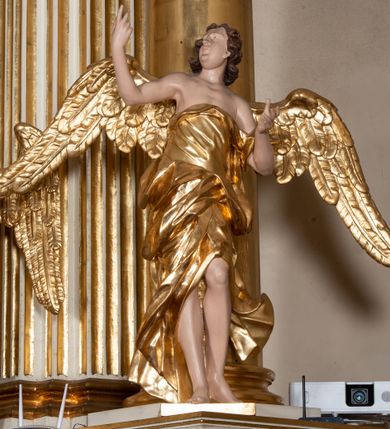 Zdjęcie nr 38: Dwukondygnacyjny, jednoosiowy ołtarz ze zwieńczeniem uzyskał strukturę architektoniczną. Stipes ołtarzowy wykonano w formie granitowego prostopadłościanu z mensą. Na mensie na osi ołtarza ustawiono tabernakulum z tronem wystawienia. Tabernakulum otrzymało kształt drewnianej skrzynki obitej blachą z drzwiczkami w formie stojącego prostokąta, z sześcioma kwaterami przedstawiającymi sceny z Pisma Świętego. Całość zamknięto silnie wysuniętym gzymsem wypukłym od frontu. Tron wystawienia utworzono w formie baldachimu ozdobionego lambrekinem z chwostami. Ujmują go spływy wolutowe z podwieszoną tkaniną, dekorowane liśćmi akantu. W przestrzeni zaplecka tronu umieszczono w promienistej glorii medalion z chrystogramem &quot;IHS&quot;. Nastawa została ustawiona na wysokim cokole, zwieńczonym profilowanym gzymsem z wyodrębnionymi dwoma wspornikami skierowanymi do wewnątrz. Retabulum ujmuje  zwrócona na zewnątrz opilastrowana para filarów, przed którymi stoi para kolumn o kapitelach kompozytowych dźwigających pełne belkowanie wyłamane na ich osi. W polu centralnym znajduje się nisza w kształcie stojącego prostokąta zwieńczonego przerwanym prostokątnie łukiem półkolistym, nadwieszonym. Niszę obramienia profilowana rama. W jej wnętrzu znajduje się obraz Wniebowzięcia Najświętsze Marii Panny w drewnianych sukienkach wotywnych. Druga kondygnacja ujęta została dwiema parami zwróconych na zewnątrz pilastrów o trzonach przechodzących w spływy wolutowe. Pilastry dźwigają gzyms wyłamany na ich osi, który w części centralnej przyjmuje kształt spłaszczonego łuku. W polu umieszczono obraz z przedstawieniem Michała Archanioła w formie stojącego prostokąta o wklęsłych, dłuższych krawędziach oraz krótszych o kształcie łuku półkolistego nadwieszonego. Nastawa zakończona została okiem Opatrzności Bożej w glorii promienistej. Na cokole przed podporami ustawiono cztery figury adorujących aniołów. Ramę w polu środkowym udekorowano ornamentem roślinnym. W górnych przyłuczach umieszczono figury puttów na obłokach. Fryz został ozdobiony kwiatowymi girlandami. Centralnie na osi na gzymsie zawieszono kartusz z monogramem Marii w polu. Na zewnętrznych krawędziach belkowania pierwszej kondygnacji siedzą dwie figury aniołów, a na spływach wolutowych cztery putta. W trzonach pilastrów drugiej kondygnacji widoczne są zwisy z ornamentem kwiatowym podwieszonym na wstążce. W polu centralnym na dole umieszczono dwa wieńce, a u góry dwie uskrzydlone główki anielskie. Na belkowaniu znajdują się dwa putta na obłokach. Struktura nastawy została polichromowana w kolorze kości słoniowej, natomiast kolumny, pilastry, profile i ornamentyka zostały wyzłocone, a obłoki posrebrzone.