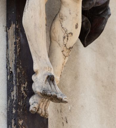 Zdjęcie nr 9: Figura Chrystusa umarłego została przybita do drewnianego krzyża za pomocą trzech gwoździ. Ciało Zbawiciela ujęto w lekkim zwisie o szeroko rozłożonych ramionach. Jego głowa bezwładnie opada na prawy bark, nogi zostały ugięte w kolanach, stopy skrzyżowane w układzie prawa na lewą.  Twarz Jezusa jest szczupła o zamkniętych oczach, prostym nosie i otwartych ustach. Okala ją krótka, silnie kręcona broda oraz długie, skręcające się w pukle i rozwiane włosy. Na głowie widoczna jest korona cierniowa. Ciało Chrystusa jest wychudzone z silnie podkreślonymi wklęsło-wypukłymi mięśniami i zaznaczonymi żebrami. Perizonium widoczne na biodrach zostało zawieszone na podwójnym sznurze odsłaniającym lewe biodro z silnie drapowaną i ekspresyjnie rozwianą tkaniną. Ciało zostało polichromowane w kolorze naturalnym, włosy i perizonium są brązowe.