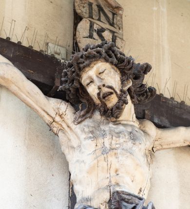 Zdjęcie nr 2: Figura Chrystusa umarłego została przybita do drewnianego krzyża za pomocą trzech gwoździ. Ciało Zbawiciela ujęto w lekkim zwisie o szeroko rozłożonych ramionach. Jego głowa bezwładnie opada na prawy bark, nogi zostały ugięte w kolanach, stopy skrzyżowane w układzie prawa na lewą.  Twarz Jezusa jest szczupła o zamkniętych oczach, prostym nosie i otwartych ustach. Okala ją krótka, silnie kręcona broda oraz długie, skręcające się w pukle i rozwiane włosy. Na głowie widoczna jest korona cierniowa. Ciało Chrystusa jest wychudzone z silnie podkreślonymi wklęsło-wypukłymi mięśniami i zaznaczonymi żebrami. Perizonium widoczne na biodrach zostało zawieszone na podwójnym sznurze odsłaniającym lewe biodro z silnie drapowaną i ekspresyjnie rozwianą tkaniną. Ciało zostało polichromowane w kolorze naturalnym, włosy i perizonium są brązowe.
