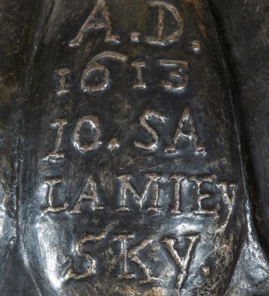 Zdjęcie nr 4: Marmurowa chrzcielnica uzyskała kształt kielicha. Na sześciennym cokole ustawiono czworoboczny postument, z którego wyrasta gruszkowa tralka podtrzymująca, spłaszczoną, sferyczną czarę dekorowaną imitacją płaskiego puklowania z wywiniętym brzegiem. Blaszana pokrywa uzyskała formę trybowanej półkuli, zakończonej aplikowaną kulą z krzyżem z gołębicą Ducha Świętego. Na pokrywie znajduje się trybowana inskrypcja: „A[NNO] D[OMINI] / 1613 /10.SA/LA MIEY/SKY&quot;.