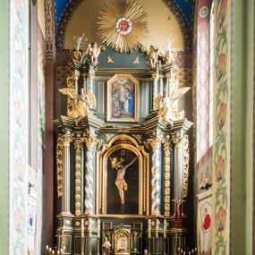 Zdjęcie nr 1: Nastawa ołtarza Ukrzyżowania uzyskała formę architektonicznego retabulum dwukondygnacyjnego, jednoosiowego ze zwieńczeniem w postaci promienistej glorii. Drewniany stipes ołtarzowy uzyskał formę prostopadłościanu podtrzymującego drewnianą mensę z marmurowym portatylem. Na mensie na osi ustawiono architektoniczne tabernakulum w formie drewnianej skrzynki na cokole, na planie trapezu o wypukłej ściance przedniej i wklęsłych ramionach. Ścianka przednia ujęta została parą zdwojonych pilastrów podtrzymujących imposty, których trzon przyjmuje formę wolut. Na ściance przedniej usytuowana została nisza obrotowa w formie stojącego prostokąta zamkniętego łukiem półkolistym nadwieszonym z uskokiem w karbowanej ramie. Widoczne pilastry dźwigają pełne belkowanie, zaś nad polem głównym wyłącznie gzyms. Drzwiczki tabernakulum ozdobiono płaskorzeźbionym przedstawieniem baranka leżącego na księdze o siedmiu pieczęciach w glorii promienistej. Retabulum ustawiono na trójstrefowym cokole. W dwóch pierwszych strefach znalazły się dwie pary wyodrębnionych prostopadłościanów stanowiących cokoły dla kolumn. Nastawę flankują dwie pary kolumn o kapitelach korynckich, spośród których wewnętrza ma skręcone trzony, a zewnętrzna kanelowane. Kolumny dźwigają pełne belkowanie wyłamane na ich osi, pod kątem, zaś nad polem środkowym wyłącznie gzyms. Niemal w całości pole główne wypełnia wnęka w formie stojącego prostokąta zamkniętego łukiem odcinkowym, nadwieszonym z uskokiem, ujęta profilowaną ramą. Wewnątrz widoczna jest mniejsza w formie stojącego prostokąta zamkniętego łukiem odcinkowym z figurą Chrystusa Ukrzyżowanego. Druga kondygnacja ustawiona jest także na cokole. Flankują ją dwie pary kolumn o kapitelach korynckich, spośród których wewnętrza ma skręcone trzony, zewnętrzna kanelowane. Kolumny dźwigają pełne belkowanie wyłamane na ich osi, pod kątem oraz fragmenty półkolistego przyczółka. W polu umieszczono obraz Zwiastowania w formie stojącego prostokąta zamkniętego trójbocznie, ujętego ramą zdobioną wolim okiem. Całość zakończona szczytem ujętym wolutami z medalionem z monogramem "IHS" w otoku z obłoków w glorii promienistej. Cokół dolny zdobiony został płycinami i rozetami. Pomiędzy kolumnami usytuowano zwisy kwiatowe na wstędze. Uszy ołtarza utworzone zostały z akantu. Fryzy występujące w retabulum dekorowany są złoconymi rozetami, zaś przyłucza ozdobiono ornamentem roślinnym. Drugą kondygnację flankują uszy utworzone z akantu i wstęgi. Na belkowaniu umieszczono siedzące figury aniołów, a na drugiej kondygnacji putta i wazony. Struktura ołtarza została polichromowana w kolorze szaro-zielonym z elementami szaro-brązowymi ze złoconymi profilami, ramami i ornamentyką, natomiast kręcone trzony posrebrzono.