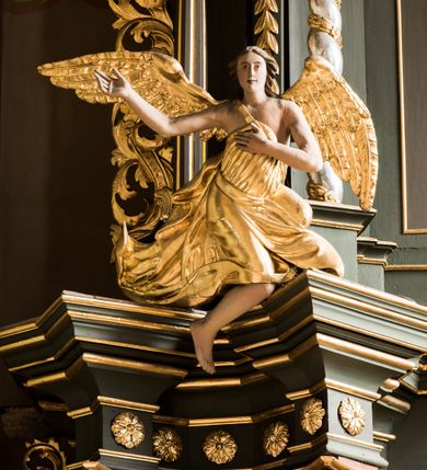 Zdjęcie nr 6: Nastawa ołtarza Ukrzyżowania uzyskała formę architektonicznego retabulum dwukondygnacyjnego, jednoosiowego ze zwieńczeniem w postaci promienistej glorii. Drewniany stipes ołtarzowy uzyskał formę prostopadłościanu podtrzymującego drewnianą mensę z marmurowym portatylem. Na mensie na osi ustawiono architektoniczne tabernakulum w formie drewnianej skrzynki na cokole, na planie trapezu o wypukłej ściance przedniej i wklęsłych ramionach. Ścianka przednia ujęta została parą zdwojonych pilastrów podtrzymujących imposty, których trzon przyjmuje formę wolut. Na ściance przedniej usytuowana została nisza obrotowa w formie stojącego prostokąta zamkniętego łukiem półkolistym nadwieszonym z uskokiem w karbowanej ramie. Widoczne pilastry dźwigają pełne belkowanie, zaś nad polem głównym wyłącznie gzyms. Drzwiczki tabernakulum ozdobiono płaskorzeźbionym przedstawieniem baranka leżącego na księdze o siedmiu pieczęciach w glorii promienistej. Retabulum ustawiono na trójstrefowym cokole. W dwóch pierwszych strefach znalazły się dwie pary wyodrębnionych prostopadłościanów stanowiących cokoły dla kolumn. Nastawę flankują dwie pary kolumn o kapitelach korynckich, spośród których wewnętrza ma skręcone trzony, a zewnętrzna kanelowane. Kolumny dźwigają pełne belkowanie wyłamane na ich osi, pod kątem, zaś nad polem środkowym wyłącznie gzyms. Niemal w całości pole główne wypełnia wnęka w formie stojącego prostokąta zamkniętego łukiem odcinkowym, nadwieszonym z uskokiem, ujęta profilowaną ramą. Wewnątrz widoczna jest mniejsza w formie stojącego prostokąta zamkniętego łukiem odcinkowym z figurą Chrystusa Ukrzyżowanego. Druga kondygnacja ustawiona jest także na cokole. Flankują ją dwie pary kolumn o kapitelach korynckich, spośród których wewnętrza ma skręcone trzony, zewnętrzna kanelowane. Kolumny dźwigają pełne belkowanie wyłamane na ich osi, pod kątem oraz fragmenty półkolistego przyczółka. W polu umieszczono obraz Zwiastowania w formie stojącego prostokąta zamkniętego trójbocznie, ujętego ramą zdobioną wolim okiem. Całość zakończona szczytem ujętym wolutami z medalionem z monogramem "IHS" w otoku z obłoków w glorii promienistej. Cokół dolny zdobiony został płycinami i rozetami. Pomiędzy kolumnami usytuowano zwisy kwiatowe na wstędze. Uszy ołtarza utworzone zostały z akantu. Fryzy występujące w retabulum dekorowany są złoconymi rozetami, zaś przyłucza ozdobiono ornamentem roślinnym. Drugą kondygnację flankują uszy utworzone z akantu i wstęgi. Na belkowaniu umieszczono siedzące figury aniołów, a na drugiej kondygnacji putta i wazony. Struktura ołtarza została polichromowana w kolorze szaro-zielonym z elementami szaro-brązowymi ze złoconymi profilami, ramami i ornamentyką, natomiast kręcone trzony posrebrzono.