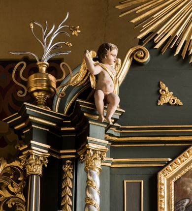 Zdjęcie nr 4: Nastawa ołtarza Ukrzyżowania uzyskała formę architektonicznego retabulum dwukondygnacyjnego, jednoosiowego ze zwieńczeniem w postaci promienistej glorii. Drewniany stipes ołtarzowy uzyskał formę prostopadłościanu podtrzymującego drewnianą mensę z marmurowym portatylem. Na mensie na osi ustawiono architektoniczne tabernakulum w formie drewnianej skrzynki na cokole, na planie trapezu o wypukłej ściance przedniej i wklęsłych ramionach. Ścianka przednia ujęta została parą zdwojonych pilastrów podtrzymujących imposty, których trzon przyjmuje formę wolut. Na ściance przedniej usytuowana została nisza obrotowa w formie stojącego prostokąta zamkniętego łukiem półkolistym nadwieszonym z uskokiem w karbowanej ramie. Widoczne pilastry dźwigają pełne belkowanie, zaś nad polem głównym wyłącznie gzyms. Drzwiczki tabernakulum ozdobiono płaskorzeźbionym przedstawieniem baranka leżącego na księdze o siedmiu pieczęciach w glorii promienistej. Retabulum ustawiono na trójstrefowym cokole. W dwóch pierwszych strefach znalazły się dwie pary wyodrębnionych prostopadłościanów stanowiących cokoły dla kolumn. Nastawę flankują dwie pary kolumn o kapitelach korynckich, spośród których wewnętrza ma skręcone trzony, a zewnętrzna kanelowane. Kolumny dźwigają pełne belkowanie wyłamane na ich osi, pod kątem, zaś nad polem środkowym wyłącznie gzyms. Niemal w całości pole główne wypełnia wnęka w formie stojącego prostokąta zamkniętego łukiem odcinkowym, nadwieszonym z uskokiem, ujęta profilowaną ramą. Wewnątrz widoczna jest mniejsza w formie stojącego prostokąta zamkniętego łukiem odcinkowym z figurą Chrystusa Ukrzyżowanego. Druga kondygnacja ustawiona jest także na cokole. Flankują ją dwie pary kolumn o kapitelach korynckich, spośród których wewnętrza ma skręcone trzony, zewnętrzna kanelowane. Kolumny dźwigają pełne belkowanie wyłamane na ich osi, pod kątem oraz fragmenty półkolistego przyczółka. W polu umieszczono obraz Zwiastowania w formie stojącego prostokąta zamkniętego trójbocznie, ujętego ramą zdobioną wolim okiem. Całość zakończona szczytem ujętym wolutami z medalionem z monogramem "IHS" w otoku z obłoków w glorii promienistej. Cokół dolny zdobiony został płycinami i rozetami. Pomiędzy kolumnami usytuowano zwisy kwiatowe na wstędze. Uszy ołtarza utworzone zostały z akantu. Fryzy występujące w retabulum dekorowany są złoconymi rozetami, zaś przyłucza ozdobiono ornamentem roślinnym. Drugą kondygnację flankują uszy utworzone z akantu i wstęgi. Na belkowaniu umieszczono siedzące figury aniołów, a na drugiej kondygnacji putta i wazony. Struktura ołtarza została polichromowana w kolorze szaro-zielonym z elementami szaro-brązowymi ze złoconymi profilami, ramami i ornamentyką, natomiast kręcone trzony posrebrzono.