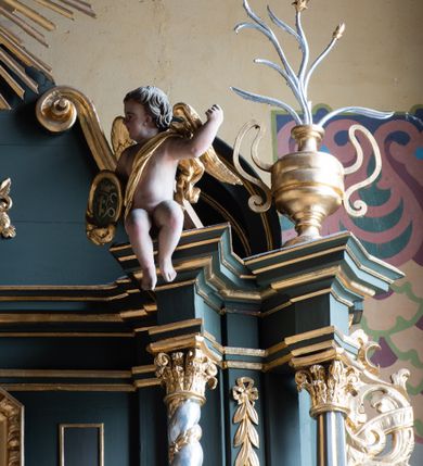 Zdjęcie nr 7: Nastawa ołtarza Ukrzyżowania uzyskała formę architektonicznego retabulum dwukondygnacyjnego, jednoosiowego ze zwieńczeniem w postaci promienistej glorii. Drewniany stipes ołtarzowy uzyskał formę prostopadłościanu podtrzymującego drewnianą mensę z marmurowym portatylem. Na mensie na osi ustawiono architektoniczne tabernakulum w formie drewnianej skrzynki na cokole, na planie trapezu o wypukłej ściance przedniej i wklęsłych ramionach. Ścianka przednia ujęta została parą zdwojonych pilastrów podtrzymujących imposty, których trzon przyjmuje formę wolut. Na ściance przedniej usytuowana została nisza obrotowa w formie stojącego prostokąta zamkniętego łukiem półkolistym nadwieszonym z uskokiem w karbowanej ramie. Widoczne pilastry dźwigają pełne belkowanie, zaś nad polem głównym wyłącznie gzyms. Drzwiczki tabernakulum ozdobiono płaskorzeźbionym przedstawieniem baranka leżącego na księdze o siedmiu pieczęciach w glorii promienistej. Retabulum ustawiono na trójstrefowym cokole. W dwóch pierwszych strefach znalazły się dwie pary wyodrębnionych prostopadłościanów stanowiących cokoły dla kolumn. Nastawę flankują dwie pary kolumn o kapitelach korynckich, spośród których wewnętrza ma skręcone trzony, a zewnętrzna kanelowane. Kolumny dźwigają pełne belkowanie wyłamane na ich osi, pod kątem, zaś nad polem środkowym wyłącznie gzyms. Niemal w całości pole główne wypełnia wnęka w formie stojącego prostokąta zamkniętego łukiem odcinkowym, nadwieszonym z uskokiem, ujęta profilowaną ramą. Wewnątrz widoczna jest mniejsza w formie stojącego prostokąta zamkniętego łukiem odcinkowym z figurą Chrystusa Ukrzyżowanego. Druga kondygnacja ustawiona jest także na cokole. Flankują ją dwie pary kolumn o kapitelach korynckich, spośród których wewnętrza ma skręcone trzony, zewnętrzna kanelowane. Kolumny dźwigają pełne belkowanie wyłamane na ich osi, pod kątem oraz fragmenty półkolistego przyczółka. W polu umieszczono obraz Zwiastowania w formie stojącego prostokąta zamkniętego trójbocznie, ujętego ramą zdobioną wolim okiem. Całość zakończona szczytem ujętym wolutami z medalionem z monogramem "IHS" w otoku z obłoków w glorii promienistej. Cokół dolny zdobiony został płycinami i rozetami. Pomiędzy kolumnami usytuowano zwisy kwiatowe na wstędze. Uszy ołtarza utworzone zostały z akantu. Fryzy występujące w retabulum dekorowany są złoconymi rozetami, zaś przyłucza ozdobiono ornamentem roślinnym. Drugą kondygnację flankują uszy utworzone z akantu i wstęgi. Na belkowaniu umieszczono siedzące figury aniołów, a na drugiej kondygnacji putta i wazony. Struktura ołtarza została polichromowana w kolorze szaro-zielonym z elementami szaro-brązowymi ze złoconymi profilami, ramami i ornamentyką, natomiast kręcone trzony posrebrzono.