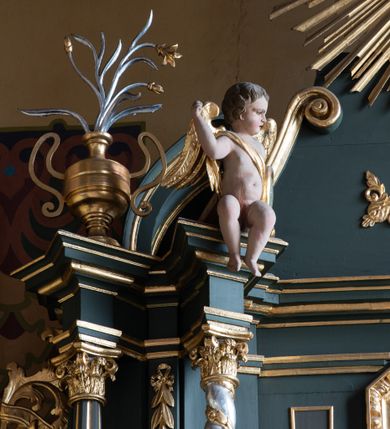 Zdjęcie nr 8: Nastawa ołtarza Ukrzyżowania uzyskała formę architektonicznego retabulum dwukondygnacyjnego, jednoosiowego ze zwieńczeniem w postaci promienistej glorii. Drewniany stipes ołtarzowy uzyskał formę prostopadłościanu podtrzymującego drewnianą mensę z marmurowym portatylem. Na mensie na osi ustawiono architektoniczne tabernakulum w formie drewnianej skrzynki na cokole, na planie trapezu o wypukłej ściance przedniej i wklęsłych ramionach. Ścianka przednia ujęta została parą zdwojonych pilastrów podtrzymujących imposty, których trzon przyjmuje formę wolut. Na ściance przedniej usytuowana została nisza obrotowa w formie stojącego prostokąta zamkniętego łukiem półkolistym nadwieszonym z uskokiem w karbowanej ramie. Widoczne pilastry dźwigają pełne belkowanie, zaś nad polem głównym wyłącznie gzyms. Drzwiczki tabernakulum ozdobiono płaskorzeźbionym przedstawieniem baranka leżącego na księdze o siedmiu pieczęciach w glorii promienistej. Retabulum ustawiono na trójstrefowym cokole. W dwóch pierwszych strefach znalazły się dwie pary wyodrębnionych prostopadłościanów stanowiących cokoły dla kolumn. Nastawę flankują dwie pary kolumn o kapitelach korynckich, spośród których wewnętrza ma skręcone trzony, a zewnętrzna kanelowane. Kolumny dźwigają pełne belkowanie wyłamane na ich osi, pod kątem, zaś nad polem środkowym wyłącznie gzyms. Niemal w całości pole główne wypełnia wnęka w formie stojącego prostokąta zamkniętego łukiem odcinkowym, nadwieszonym z uskokiem, ujęta profilowaną ramą. Wewnątrz widoczna jest mniejsza w formie stojącego prostokąta zamkniętego łukiem odcinkowym z figurą Chrystusa Ukrzyżowanego. Druga kondygnacja ustawiona jest także na cokole. Flankują ją dwie pary kolumn o kapitelach korynckich, spośród których wewnętrza ma skręcone trzony, zewnętrzna kanelowane. Kolumny dźwigają pełne belkowanie wyłamane na ich osi, pod kątem oraz fragmenty półkolistego przyczółka. W polu umieszczono obraz Zwiastowania w formie stojącego prostokąta zamkniętego trójbocznie, ujętego ramą zdobioną wolim okiem. Całość zakończona szczytem ujętym wolutami z medalionem z monogramem "IHS" w otoku z obłoków w glorii promienistej. Cokół dolny zdobiony został płycinami i rozetami. Pomiędzy kolumnami usytuowano zwisy kwiatowe na wstędze. Uszy ołtarza utworzone zostały z akantu. Fryzy występujące w retabulum dekorowany są złoconymi rozetami, zaś przyłucza ozdobiono ornamentem roślinnym. Drugą kondygnację flankują uszy utworzone z akantu i wstęgi. Na belkowaniu umieszczono siedzące figury aniołów, a na drugiej kondygnacji putta i wazony. Struktura ołtarza została polichromowana w kolorze szaro-zielonym z elementami szaro-brązowymi ze złoconymi profilami, ramami i ornamentyką, natomiast kręcone trzony posrebrzono.