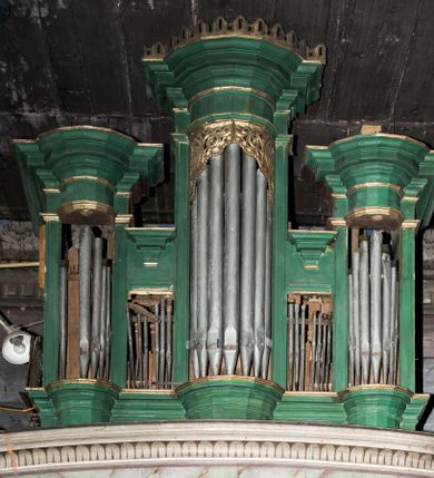 Zdjęcie nr 1: Architektoniczny prospekt organowy uzyskał pięcioosiowe założenie jednokondygnacyjne ustawione na wysokim cokole. Osie pierwsza, trzecia i piąta z większymi piszczałkami są wypukłe. Pierwsza i piąta są niższe od trzeciej. Wszystkie zwieńczone zostały pełnym belkowaniem z wydatnym, profilowanym gzymsem. W osi środkowej dodatkowo znalazł się ażurowy, złocony lambrekin oraz ornament ze złoconej wici roślinnej. Osie parzyste są niższe z płaskimi, prostokątnymi niszami mieszczącymi mniejsze piszczałki. Wieńczą je profilowano-fazowane konsole. Struktura prospektu została polichromowana w odcieniach morskiej zieleni, zaś ornamentyka i załamania profili architektonicznych wyzłocono.