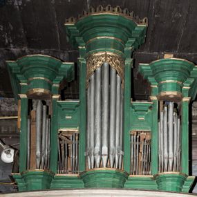 Zdjęcie nr 1: Architektoniczny prospekt organowy uzyskał pięcioosiowe założenie jednokondygnacyjne ustawione na wysokim cokole. Osie pierwsza, trzecia i piąta z większymi piszczałkami są wypukłe. Pierwsza i piąta są niższe od trzeciej. Wszystkie zwieńczone zostały pełnym belkowaniem z wydatnym, profilowanym gzymsem. W osi środkowej dodatkowo znalazł się ażurowy, złocony lambrekin oraz ornament ze złoconej wici roślinnej. Osie parzyste są niższe z płaskimi, prostokątnymi niszami mieszczącymi mniejsze piszczałki. Wieńczą je profilowano-fazowane konsole. Struktura prospektu została polichromowana w odcieniach morskiej zieleni, zaś ornamentyka i załamania profili architektonicznych wyzłocono.