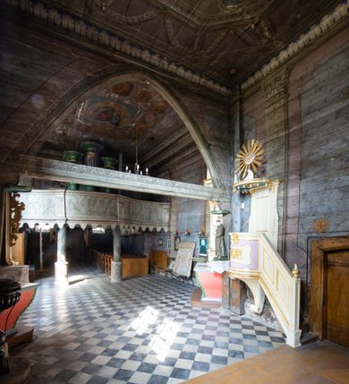 Zdjęcie nr 4: Architektoniczny prospekt organowy uzyskał pięcioosiowe założenie jednokondygnacyjne ustawione na wysokim cokole. Osie pierwsza, trzecia i piąta z większymi piszczałkami są wypukłe. Pierwsza i piąta są niższe od trzeciej. Wszystkie zwieńczone zostały pełnym belkowaniem z wydatnym, profilowanym gzymsem. W osi środkowej dodatkowo znalazł się ażurowy, złocony lambrekin oraz ornament ze złoconej wici roślinnej. Osie parzyste są niższe z płaskimi, prostokątnymi niszami mieszczącymi mniejsze piszczałki. Wieńczą je profilowano-fazowane konsole. Struktura prospektu została polichromowana w odcieniach morskiej zieleni, zaś ornamentyka i załamania profili architektonicznych wyzłocono.