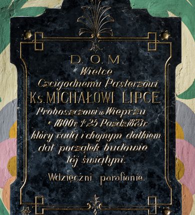 Zdjęcie nr 1: Epitafium uzyskało kształt stojącego prostokąta, zwieńczoną   łukiem półkolistym, nadwieszonym z uskokiem. Na bocznych krawędziach płyciny widoczne są wcięcia. W jej polu obwiedzionym ornamentem liniowym ze stylizowaną gałązka palmową na osi ryty tekst: "D[EO] O[PTIMO] M[AXIMO] / Wielce / Czcigodnemu Pasterzowi / Ks[iędzu][ MICHAŁOWI LIPCE / Proboszczowi w Wieprzu / * 1800 r[oku] + 25 Paźdz[iernika] 1873 r[oku] / który radą i chojnym datkiem / dał początek budowie / tej świątyni. / Wdzięczni parafianie". W czterech narożach umieszczono ozdobne gwoździe ze żłobionym motywem sześcioramiennej gwiazdy wokół.