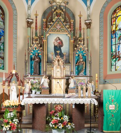 Zdjęcie nr 1: Wolnostojący, jednokondygnacyjny, trójosiowy ołtarz uzyskał formę architektoniczną ze zwieńczeniem. Stipes ołtarzowy przyjął formę leżącego prostopadłościanu ustawionego na podeście z dwoma gradusami, na którym wsparto drewnianą mensę z portatylem. Fronton stipesu podzielono za pomocą trzech płyciny, czworoboczną na osi, a w osiach skrajnych prostokątnymi. W płycinie pola środkowego umieszczono płaskorzeźbiony krzyż równoramienny wpisany w okręg. Natomiast w polach bocznych znalazły się ostrołukowe arkadki wypełnione malowanym i złoconym ornamentem roślinno-kwiatowym. Na mensie na osi ustawiono architektoniczne tabernakulum z tronem eucharystycznym. Jego dwuskrzydłowe drzwi ujęte zostały parą lizen, których płyciny wypełniono płaskorzeźbionym ornamentem. Drzwiczki ozdobiono płaskorzeźbioną dekoracją z winną latoroślą i srebrnymi literami „A” i „Ω”. Na lizenach wsparto niewielki, fazowany gzyms. Ponad nim usytuowano tron eucharystyczny w formie aediculi flankowanej złoconymi kolumnami na postumentach z liściastymi kapitelami podtrzymującymi imposty przechodzące w pinakle z kwiatonami. Pomiędzy nimi znalazła się wimperga z czołganiami i wieńczącym ją pinaklem z kwiatonem. Wimpergę wypełnia stylizowany łuk trójlistny. W niszy na tylnej ściance wykonano malarską dekorację z przedstawionym kielichem z jaśniejącym nad nim Najświętszym Sercem Pana Jezusa w koronie cierniowej, na tle dekoracji roślinnej. Całoś baldachimu nakrywa daszek siodłowy. Tabernakulum flankują dwa adorujące anioły w jasnych szatach ustawione na profilowanych postumentach dekorowanych na licu łacińskimi napisami "Adoremus" i "Venite". Nastawa ołtarzowa ustawiona została na wysokim, dwustrefowym cokole. Górną strefę artykułowano za pomocą czworobocznych, zielonych płycin wypełnionych płaskorzeźbionym i złoconym ornamentem roślinnym, obramienionych profilowanymi listwami. Cokół zwieńczony został profilowanym gzymsem. Część środkowa nastawy jest wyższa i szersza od osi bocznych. Tworzy ją pole w kształcie stojącego prostokąta zamknięte u góry łukiem siodłowym, ujętego złoconą, profilowaną ramą. Pole flankują dwie smukłe kolumienki z liściastymi kapitelami, ustawione na postumentach, przechodzące w pinakle zwieńczone kwiatonami. Pomiędzy pinaklami usytuowano wimpergę wypełnioną maswerkiem z czterolistnym polem, w którym znajduje się napis:"S[anc]t[us] Mrtinus". Wimpergę zakończoną pinaklem z kwiatonem zdobią czołgani. Ponad nią wypiętrzone zostało ażurowe zwieńczenie utworzone z podwójnych ostrołukowych arkadek flankujących fialę z kwiatonem. W polu kondygnacji prezentowany jest obraz ze św. Marcinem oraz dwa pozostałe na zasuwie z przedstawienie Madonny Sykstyńskiej oraz Matki Boskiej Nieustającej Pomocy. Poniżej pola obrazowego wprowadzono płycinę w kształcie leżącego prostokąta, dekorowaną malowaną, złoconą ornamentyką na zielonym tle. W osiach bocznych znalazły się dwie aedicule zwieńczone wimpergami z czołgankami i kwiatonem, flankowane parą wysmuklonych pinakli z kwiatonami. Górną część aediculi wypełnia arkatura. W niszach na niebieskim tle ze złotymi gwiazdami ustawiono figury św. Franciszka z Asyżu i św. Elżbiety z Turyngii. Kondygnację flankują ażurowe struktury utworzone z płycin ujętych smukłymi pinaklami, wypełnionymi płaskorzeźbionym ornamentem roślinnym. Struktura ołtarza polichromowana została w odcieniach zgaszonego brązu. Załamania profili architektonicznych pomalowano na czerwono, zielono i niebiesko, natomiast ornamenty wyzłocono. 