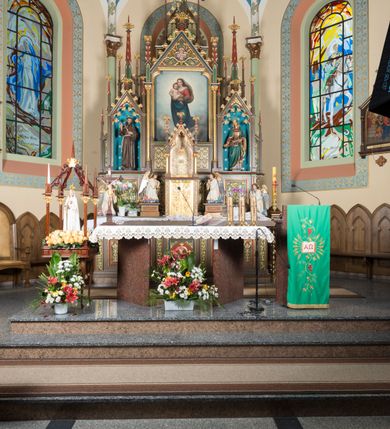 Zdjęcie nr 7: Wolnostojący, jednokondygnacyjny, trójosiowy ołtarz uzyskał formę architektoniczną ze zwieńczeniem. Stipes ołtarzowy przyjął formę leżącego prostopadłościanu ustawionego na podeście z dwoma gradusami, na którym wsparto drewnianą mensę z portatylem. Fronton stipesu podzielono za pomocą trzech płyciny, czworoboczną na osi, a w osiach skrajnych prostokątnymi. W płycinie pola środkowego umieszczono płaskorzeźbiony krzyż równoramienny wpisany w okręg. Natomiast w polach bocznych znalazły się ostrołukowe arkadki wypełnione malowanym i złoconym ornamentem roślinno-kwiatowym. Na mensie na osi ustawiono architektoniczne tabernakulum z tronem eucharystycznym. Jego dwuskrzydłowe drzwi ujęte zostały parą lizen, których płyciny wypełniono płaskorzeźbionym ornamentem. Drzwiczki ozdobiono płaskorzeźbioną dekoracją z winną latoroślą i srebrnymi literami „A” i „Ω”. Na lizenach wsparto niewielki, fazowany gzyms. Ponad nim usytuowano tron eucharystyczny w formie aediculi flankowanej złoconymi kolumnami na postumentach z liściastymi kapitelami podtrzymującymi imposty przechodzące w pinakle z kwiatonami. Pomiędzy nimi znalazła się wimperga z czołganiami i wieńczącym ją pinaklem z kwiatonem. Wimpergę wypełnia stylizowany łuk trójlistny. W niszy na tylnej ściance wykonano malarską dekorację z przedstawionym kielichem z jaśniejącym nad nim Najświętszym Sercem Pana Jezusa w koronie cierniowej, na tle dekoracji roślinnej. Całoś baldachimu nakrywa daszek siodłowy. Tabernakulum flankują dwa adorujące anioły w jasnych szatach ustawione na profilowanych postumentach dekorowanych na licu łacińskimi napisami "Adoremus" i "Venite". Nastawa ołtarzowa ustawiona została na wysokim, dwustrefowym cokole. Górną strefę artykułowano za pomocą czworobocznych, zielonych płycin wypełnionych płaskorzeźbionym i złoconym ornamentem roślinnym, obramienionych profilowanymi listwami. Cokół zwieńczony został profilowanym gzymsem. Część środkowa nastawy jest wyższa i szersza od osi bocznych. Tworzy ją pole w kształcie stojącego prostokąta zamknięte u góry łukiem siodłowym, ujętego złoconą, profilowaną ramą. Pole flankują dwie smukłe kolumienki z liściastymi kapitelami, ustawione na postumentach, przechodzące w pinakle zwieńczone kwiatonami. Pomiędzy pinaklami usytuowano wimpergę wypełnioną maswerkiem z czterolistnym polem, w którym znajduje się napis:"S[anc]t[us] Mrtinus". Wimpergę zakończoną pinaklem z kwiatonem zdobią czołgani. Ponad nią wypiętrzone zostało ażurowe zwieńczenie utworzone z podwójnych ostrołukowych arkadek flankujących fialę z kwiatonem. W polu kondygnacji prezentowany jest obraz ze św. Marcinem oraz dwa pozostałe na zasuwie z przedstawienie Madonny Sykstyńskiej oraz Matki Boskiej Nieustającej Pomocy. Poniżej pola obrazowego wprowadzono płycinę w kształcie leżącego prostokąta, dekorowaną malowaną, złoconą ornamentyką na zielonym tle. W osiach bocznych znalazły się dwie aedicule zwieńczone wimpergami z czołgankami i kwiatonem, flankowane parą wysmuklonych pinakli z kwiatonami. Górną część aediculi wypełnia arkatura. W niszach na niebieskim tle ze złotymi gwiazdami ustawiono figury św. Franciszka z Asyżu i św. Elżbiety z Turyngii. Kondygnację flankują ażurowe struktury utworzone z płycin ujętych smukłymi pinaklami, wypełnionymi płaskorzeźbionym ornamentem roślinnym. Struktura ołtarza polichromowana została w odcieniach zgaszonego brązu. Załamania profili architektonicznych pomalowano na czerwono, zielono i niebiesko, natomiast ornamenty wyzłocono. 