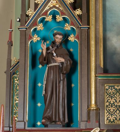 Zdjęcie nr 13: Wolnostojący, jednokondygnacyjny, trójosiowy ołtarz uzyskał formę architektoniczną ze zwieńczeniem. Stipes ołtarzowy przyjął formę leżącego prostopadłościanu ustawionego na podeście z dwoma gradusami, na którym wsparto drewnianą mensę z portatylem. Fronton stipesu podzielono za pomocą trzech płyciny, czworoboczną na osi, a w osiach skrajnych prostokątnymi. W płycinie pola środkowego umieszczono płaskorzeźbiony krzyż równoramienny wpisany w okręg. Natomiast w polach bocznych znalazły się ostrołukowe arkadki wypełnione malowanym i złoconym ornamentem roślinno-kwiatowym. Na mensie na osi ustawiono architektoniczne tabernakulum z tronem eucharystycznym. Jego dwuskrzydłowe drzwi ujęte zostały parą lizen, których płyciny wypełniono płaskorzeźbionym ornamentem. Drzwiczki ozdobiono płaskorzeźbioną dekoracją z winną latoroślą i srebrnymi literami „A” i „Ω”. Na lizenach wsparto niewielki, fazowany gzyms. Ponad nim usytuowano tron eucharystyczny w formie aediculi flankowanej złoconymi kolumnami na postumentach z liściastymi kapitelami podtrzymującymi imposty przechodzące w pinakle z kwiatonami. Pomiędzy nimi znalazła się wimperga z czołganiami i wieńczącym ją pinaklem z kwiatonem. Wimpergę wypełnia stylizowany łuk trójlistny. W niszy na tylnej ściance wykonano malarską dekorację z przedstawionym kielichem z jaśniejącym nad nim Najświętszym Sercem Pana Jezusa w koronie cierniowej, na tle dekoracji roślinnej. Całoś baldachimu nakrywa daszek siodłowy. Tabernakulum flankują dwa adorujące anioły w jasnych szatach ustawione na profilowanych postumentach dekorowanych na licu łacińskimi napisami "Adoremus" i "Venite". Nastawa ołtarzowa ustawiona została na wysokim, dwustrefowym cokole. Górną strefę artykułowano za pomocą czworobocznych, zielonych płycin wypełnionych płaskorzeźbionym i złoconym ornamentem roślinnym, obramienionych profilowanymi listwami. Cokół zwieńczony został profilowanym gzymsem. Część środkowa nastawy jest wyższa i szersza od osi bocznych. Tworzy ją pole w kształcie stojącego prostokąta zamknięte u góry łukiem siodłowym, ujętego złoconą, profilowaną ramą. Pole flankują dwie smukłe kolumienki z liściastymi kapitelami, ustawione na postumentach, przechodzące w pinakle zwieńczone kwiatonami. Pomiędzy pinaklami usytuowano wimpergę wypełnioną maswerkiem z czterolistnym polem, w którym znajduje się napis:"S[anc]t[us] Mrtinus". Wimpergę zakończoną pinaklem z kwiatonem zdobią czołgani. Ponad nią wypiętrzone zostało ażurowe zwieńczenie utworzone z podwójnych ostrołukowych arkadek flankujących fialę z kwiatonem. W polu kondygnacji prezentowany jest obraz ze św. Marcinem oraz dwa pozostałe na zasuwie z przedstawienie Madonny Sykstyńskiej oraz Matki Boskiej Nieustającej Pomocy. Poniżej pola obrazowego wprowadzono płycinę w kształcie leżącego prostokąta, dekorowaną malowaną, złoconą ornamentyką na zielonym tle. W osiach bocznych znalazły się dwie aedicule zwieńczone wimpergami z czołgankami i kwiatonem, flankowane parą wysmuklonych pinakli z kwiatonami. Górną część aediculi wypełnia arkatura. W niszach na niebieskim tle ze złotymi gwiazdami ustawiono figury św. Franciszka z Asyżu i św. Elżbiety z Turyngii. Kondygnację flankują ażurowe struktury utworzone z płycin ujętych smukłymi pinaklami, wypełnionymi płaskorzeźbionym ornamentem roślinnym. Struktura ołtarza polichromowana została w odcieniach zgaszonego brązu. Załamania profili architektonicznych pomalowano na czerwono, zielono i niebiesko, natomiast ornamenty wyzłocono. 