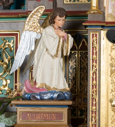 Zdjęcie nr 3: Wolnostojący, jednokondygnacyjny, trójosiowy ołtarz uzyskał formę architektoniczną ze zwieńczeniem. Stipes ołtarzowy przyjął formę leżącego prostopadłościanu ustawionego na podeście z dwoma gradusami, na którym wsparto drewnianą mensę z portatylem. Fronton stipesu podzielono za pomocą trzech płyciny, czworoboczną na osi, a w osiach skrajnych prostokątnymi. W płycinie pola środkowego umieszczono płaskorzeźbiony krzyż równoramienny wpisany w okręg. Natomiast w polach bocznych znalazły się ostrołukowe arkadki wypełnione malowanym i złoconym ornamentem roślinno-kwiatowym. Na mensie na osi ustawiono architektoniczne tabernakulum z tronem eucharystycznym. Jego dwuskrzydłowe drzwi ujęte zostały parą lizen, których płyciny wypełniono płaskorzeźbionym ornamentem. Drzwiczki ozdobiono płaskorzeźbioną dekoracją z winną latoroślą i srebrnymi literami „A” i „Ω”. Na lizenach wsparto niewielki, fazowany gzyms. Ponad nim usytuowano tron eucharystyczny w formie aediculi flankowanej złoconymi kolumnami na postumentach z liściastymi kapitelami podtrzymującymi imposty przechodzące w pinakle z kwiatonami. Pomiędzy nimi znalazła się wimperga z czołganiami i wieńczącym ją pinaklem z kwiatonem. Wimpergę wypełnia stylizowany łuk trójlistny. W niszy na tylnej ściance wykonano malarską dekorację z przedstawionym kielichem z jaśniejącym nad nim Najświętszym Sercem Pana Jezusa w koronie cierniowej, na tle dekoracji roślinnej. Całoś baldachimu nakrywa daszek siodłowy. Tabernakulum flankują dwa adorujące anioły w jasnych szatach ustawione na profilowanych postumentach dekorowanych na licu łacińskimi napisami "Adoremus" i "Venite". Nastawa ołtarzowa ustawiona została na wysokim, dwustrefowym cokole. Górną strefę artykułowano za pomocą czworobocznych, zielonych płycin wypełnionych płaskorzeźbionym i złoconym ornamentem roślinnym, obramienionych profilowanymi listwami. Cokół zwieńczony został profilowanym gzymsem. Część środkowa nastawy jest wyższa i szersza od osi bocznych. Tworzy ją pole w kształcie stojącego prostokąta zamknięte u góry łukiem siodłowym, ujętego złoconą, profilowaną ramą. Pole flankują dwie smukłe kolumienki z liściastymi kapitelami, ustawione na postumentach, przechodzące w pinakle zwieńczone kwiatonami. Pomiędzy pinaklami usytuowano wimpergę wypełnioną maswerkiem z czterolistnym polem, w którym znajduje się napis:"S[anc]t[us] Mrtinus". Wimpergę zakończoną pinaklem z kwiatonem zdobią czołgani. Ponad nią wypiętrzone zostało ażurowe zwieńczenie utworzone z podwójnych ostrołukowych arkadek flankujących fialę z kwiatonem. W polu kondygnacji prezentowany jest obraz ze św. Marcinem oraz dwa pozostałe na zasuwie z przedstawienie Madonny Sykstyńskiej oraz Matki Boskiej Nieustającej Pomocy. Poniżej pola obrazowego wprowadzono płycinę w kształcie leżącego prostokąta, dekorowaną malowaną, złoconą ornamentyką na zielonym tle. W osiach bocznych znalazły się dwie aedicule zwieńczone wimpergami z czołgankami i kwiatonem, flankowane parą wysmuklonych pinakli z kwiatonami. Górną część aediculi wypełnia arkatura. W niszach na niebieskim tle ze złotymi gwiazdami ustawiono figury św. Franciszka z Asyżu i św. Elżbiety z Turyngii. Kondygnację flankują ażurowe struktury utworzone z płycin ujętych smukłymi pinaklami, wypełnionymi płaskorzeźbionym ornamentem roślinnym. Struktura ołtarza polichromowana została w odcieniach zgaszonego brązu. Załamania profili architektonicznych pomalowano na czerwono, zielono i niebiesko, natomiast ornamenty wyzłocono. 