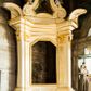 Zdjęcie nr 1: Jednokondygnacyjna i jednoosiowa nastawa ołtarza bocznego uzyskała formę architektoniczną ze zwieńczeniem, ustawioną na cokole. Stipes ołtarzowy ustawiony na podeście uzyskał kształt sarkofagu malowanego na czerwono o linii wklęsło-wypukłej z profilowanym cokołem i gzymsem pomalowanych na bladoniebiesko. W narożach stipesu dekorację wykonano na zielono w geometryczne wzory. W centrum pola umieszczono malowany chrystogram "IHS" na niebieskim tle otoczony wieńcem z kwiatów. Nastawa została ujęta parą opilastrowanych filarów, ustawionych pod kątem, zwróconych na zewnątrz, dźwigających pełne belkowanie przerwane nad polem środkowym oraz fragmenty przerwanego odwróconego przyczółka. Trzony wewnętrznych pilastrów o głowicach korynckich są kanelowane. W polu głównym znajduje się prześwit w formie stojącego prostokąta zamkniętego trójbocznie. Pilastry zewnętrzne u szczytu zwieńczono złoconymi wolutami. Zwieńczenie uzyskało formę trapezu o wklęsłych bokach zakończonego półkoliście wygiętym gzymsem, przechodzącym po bokach w woluty. Na wolutach widoczne są liście palmowe. W polu umieszczono obraz św. Erazma w profilowanej ramie w formie zbliżonej do trapezu o wklęsłych bokach i ściętych dolnych narożach, zamkniętego łukiem falistym. Struktura nastawy została polichromowana w kolorze kości słoniowej, ze złoconymi profilami i ornamentami.


