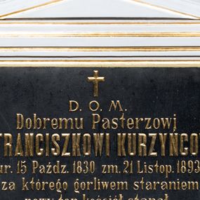 Zdjęcie nr 1: Epitafium uzyskało formę płyty marmurowej w kształcie leżącego prostokąta, ujętej w architektoniczne obramienie. Obramowanie składa się z konsoli w kształcie profilowanego belkowania wyłamanego w osiach skrajnych, na której wsparto cokół podtrzymujący dwa pilastry z kanelowanymi trzonami i głowicami zdobionymi stylizowanymi, złoconymi liśćmi. Podpory podtrzymują belkowanie z trójkątnym przyczółkiem zwieńczonym krzyżem. Tablicę epitafijną wypełnia złocony, ryty tekst: ,,D[EO] O[PTIMO] M[AXIMO] / Dobremu Pasterzowi / X[ędzu]. FRANCISZKOWI KURZYŃCOWI / ur. 15 Paźdz[ernika] 1830 zm. 21 Listop[ada] 1893 / za którego gorliwem staraniem / nowy ten kościół stanął, /z obowiązany szczery przyjaciel”. W prawy dolnym roku ramy umieszczono sygnaturę autora epitafium: ,,J. Kulesza w Krakowie”.