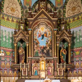 Zdjęcie nr 1: Ołtarz główny uzyskał formę architektonicznej struktury przyściennej, trójosiowej i jednokondygnacyjnej ze zwieńczeniem. Stipes ołtarzowy przyjął formę stołu, gdzie mensę z portatylem wsparto na czterech kolumnach ustawionych na wysokich wielobocznych bazach. Pomiędzy nimi usytuowano płaskorzeźbioną sceną Ostatniej Wieczerzy w kształcie leżącego prostokąta. Na mensie w osi ołtarza ustawione zostało tabernakulum z tronem wystawienia w kształcie baldachimu, stanowiące cześć środkową architektonicznego, trójosiowego założenia, gdzie w osiach bocznych w półokrągłych aediculach z wimpergami ustawiono parę adorujących aniołów. Nastawa ustawiona na wysokim cokole została dekorowana profilowanymi płycinami, ponad którymi poprowadzono profilowanym gzyms. Oś środkowa retabulum została ujęta złoconymi kolumnami o korynckich kapitelach i gładkich trzonach. Kolumny dźwigają półkoliście zamkniętą arkadę zwieńczoną profilowanym gzymsem z trójkątnie zakończoną wimpergą ozdobioną żabkami. Zwieńczenie utworzono w formie ażurowej kapliczki na rzucie wieloboku mieszczącej pełnoplastyczną figurę Michała Archanioła trzymającego miecz i wagę. Kapliczkę zakończono wieloboczną fialą o ściankach zdobionych ślepymi maswerkami. W osiach skrajnych wykonano analogiczne arkady wsparte na złoconych kolumnach mieszczące figury św. Piotra (z lewej) i św. Pawła (z prawej). W zwieńczeniach w osi znalazły się w ażurowych kapliczkach zakończonych fialami pełnoplastyczne figury św. Wojciecha i św. Stanisława w strojach pontyfikalnych. W polu ołtarza usytuowano obraz przedstawiający wszystkich świętych adorujących Trójcę Przenajświętszą. Pole ujmuje płaskorzeźbiona, złocona rama z dekoracją akantową zamknięta łukiem trójlistnym. W podłuczu wykonano arkaturę. Na zasuwie umieszczono obraz Najświętszego Serca Pana Jezusa. W płycinach wypełniających elementy architektoniczne znalazła się stylizowana dekoracja akantowa oraz motyw czwórliścia wpisanego w okrąg. Struktura ołtarza została polichromowana w odcieniach zgaszonej czerwieni i złamanego brązu wchodzącego w fiolet. Ornamentyka oraz detale elementów i profilów architektonicznych wyzłocono.