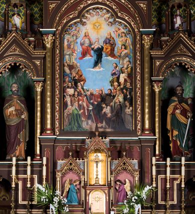 Zdjęcie nr 5: Ołtarz główny uzyskał formę architektonicznej struktury przyściennej, trójosiowej i jednokondygnacyjnej ze zwieńczeniem. Stipes ołtarzowy przyjął formę stołu, gdzie mensę z portatylem wsparto na czterech kolumnach ustawionych na wysokich wielobocznych bazach. Pomiędzy nimi usytuowano płaskorzeźbioną sceną Ostatniej Wieczerzy w kształcie leżącego prostokąta. Na mensie w osi ołtarza ustawione zostało tabernakulum z tronem wystawienia w kształcie baldachimu, stanowiące cześć środkową architektonicznego, trójosiowego założenia, gdzie w osiach bocznych w półokrągłych aediculach z wimpergami ustawiono parę adorujących aniołów. Nastawa ustawiona na wysokim cokole została dekorowana profilowanymi płycinami, ponad którymi poprowadzono profilowanym gzyms. Oś środkowa retabulum została ujęta złoconymi kolumnami o korynckich kapitelach i gładkich trzonach. Kolumny dźwigają półkoliście zamkniętą arkadę zwieńczoną profilowanym gzymsem z trójkątnie zakończoną wimpergą ozdobioną żabkami. Zwieńczenie utworzono w formie ażurowej kapliczki na rzucie wieloboku mieszczącej pełnoplastyczną figurę Michała Archanioła trzymającego miecz i wagę. Kapliczkę zakończono wieloboczną fialą o ściankach zdobionych ślepymi maswerkami. W osiach skrajnych wykonano analogiczne arkady wsparte na złoconych kolumnach mieszczące figury św. Piotra (z lewej) i św. Pawła (z prawej). W zwieńczeniach w osi znalazły się w ażurowych kapliczkach zakończonych fialami pełnoplastyczne figury św. Wojciecha i św. Stanisława w strojach pontyfikalnych. W polu ołtarza usytuowano obraz przedstawiający wszystkich świętych adorujących Trójcę Przenajświętszą. Pole ujmuje płaskorzeźbiona, złocona rama z dekoracją akantową zamknięta łukiem trójlistnym. W podłuczu wykonano arkaturę. Na zasuwie umieszczono obraz Najświętszego Serca Pana Jezusa. W płycinach wypełniających elementy architektoniczne znalazła się stylizowana dekoracja akantowa oraz motyw czwórliścia wpisanego w okrąg. Struktura ołtarza została polichromowana w odcieniach zgaszonej czerwieni i złamanego brązu wchodzącego w fiolet. Ornamentyka oraz detale elementów i profilów architektonicznych wyzłocono.